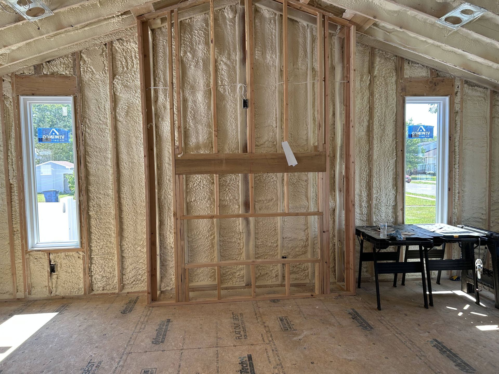 Partially insulated room under construction with exposed studs, windows, and a table by the wall