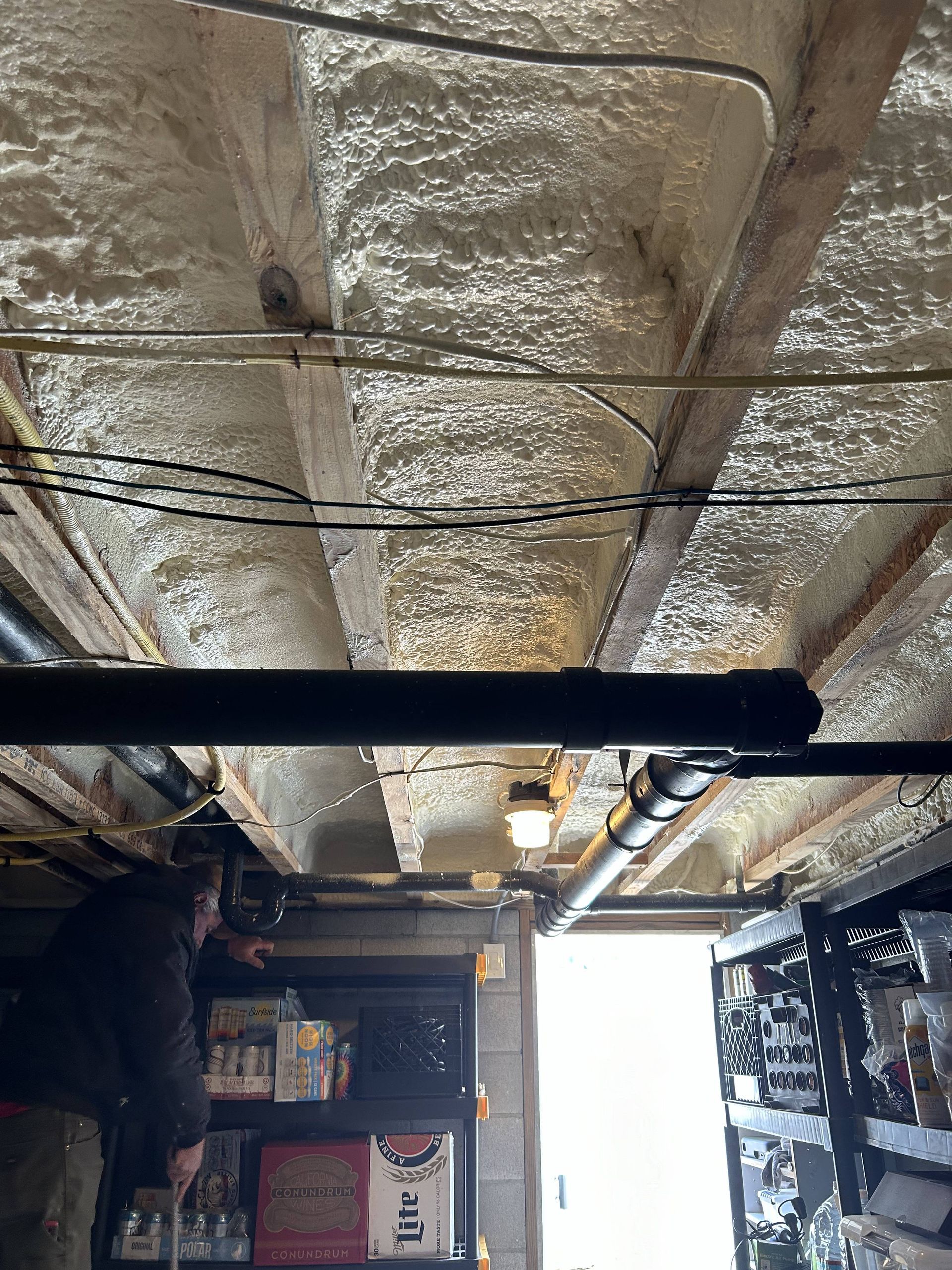Basement ceiling with exposed insulation, pipes, and shelving in a storage area