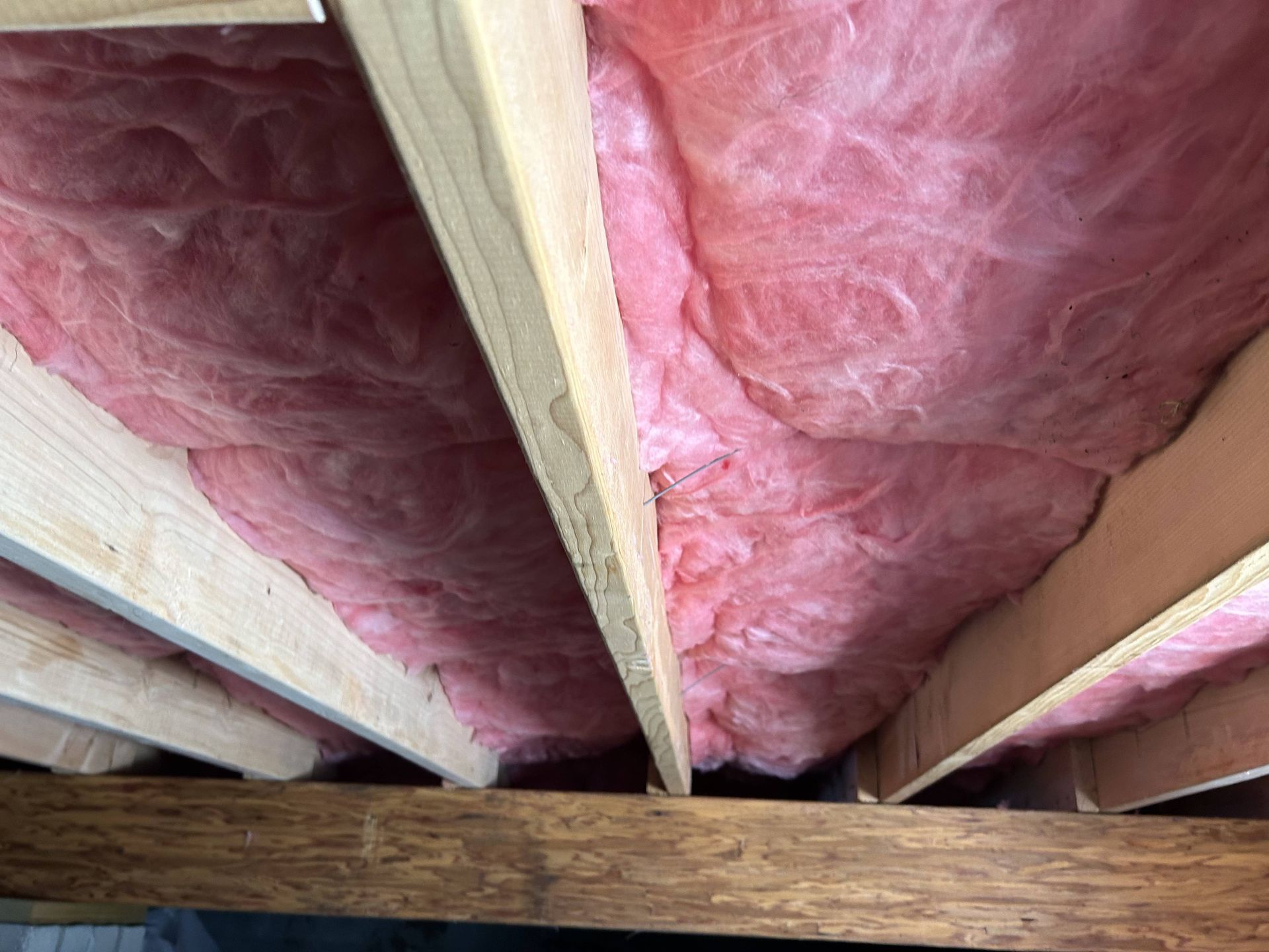 Pink fiberglass insulation between wooden ceiling joists in an unfinished attic