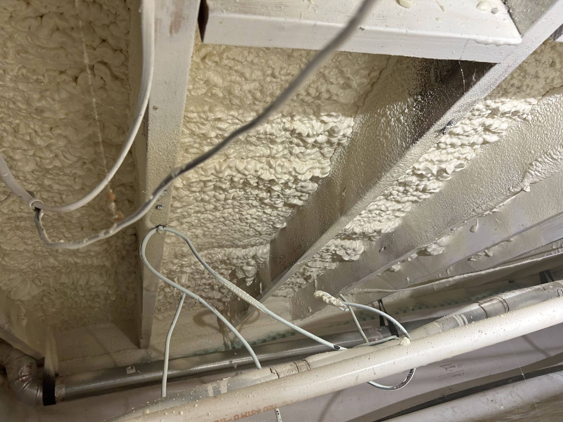 Exposed ceiling beams with spray foam insulation and loose electrical wires in an unfinished room