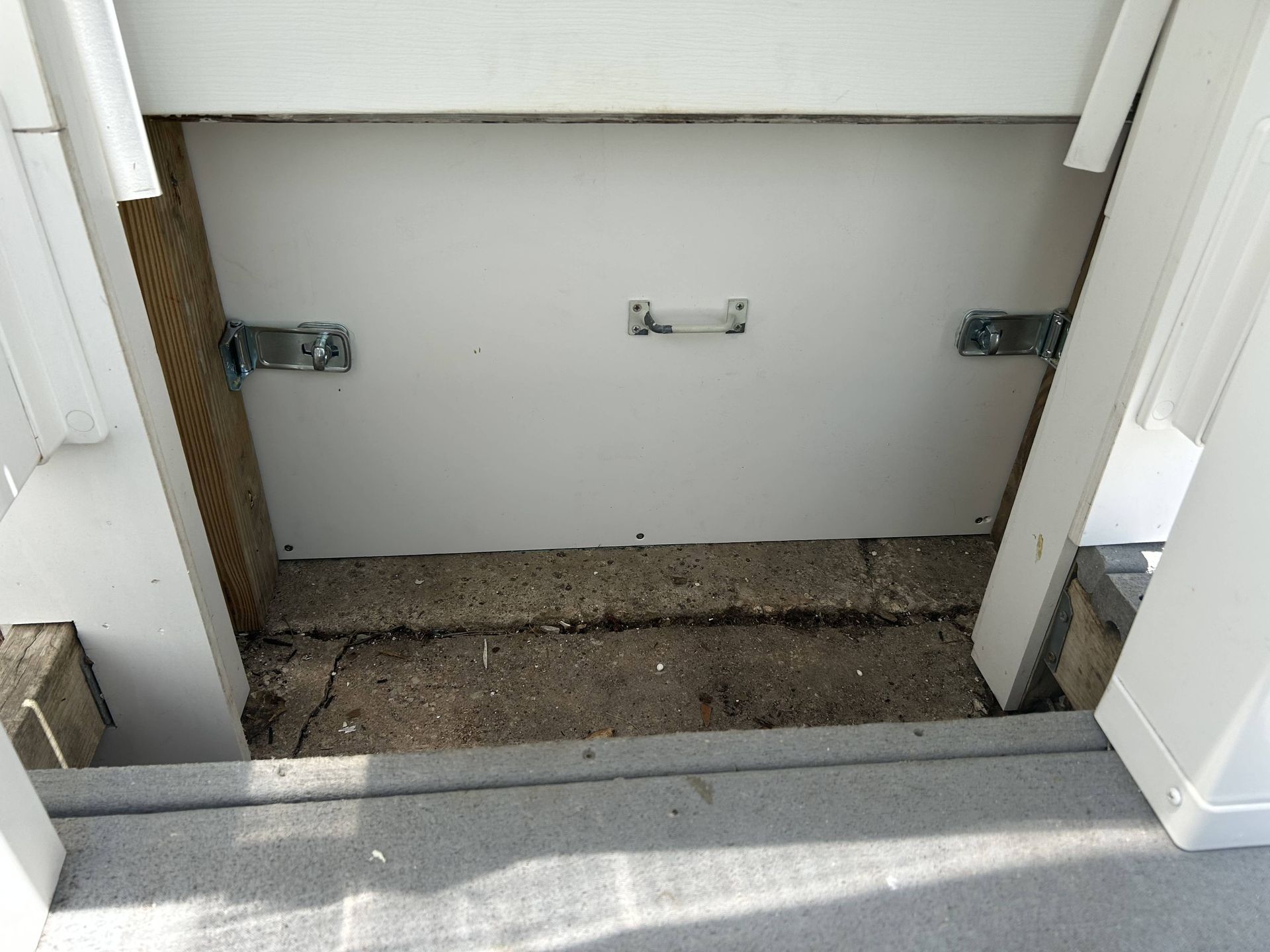 Empty wall cavity with metal brackets and a dirt floor between white structural panels