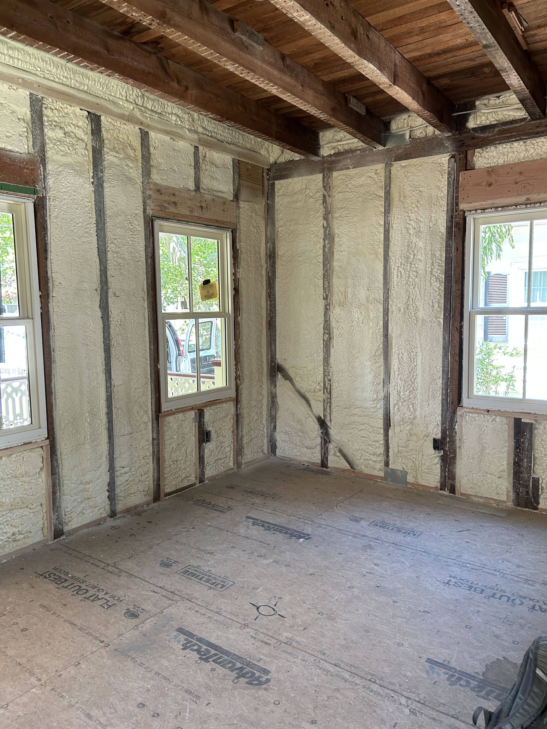 Unfinished room with exposed beams, insulated walls, and two windows letting in daylight.