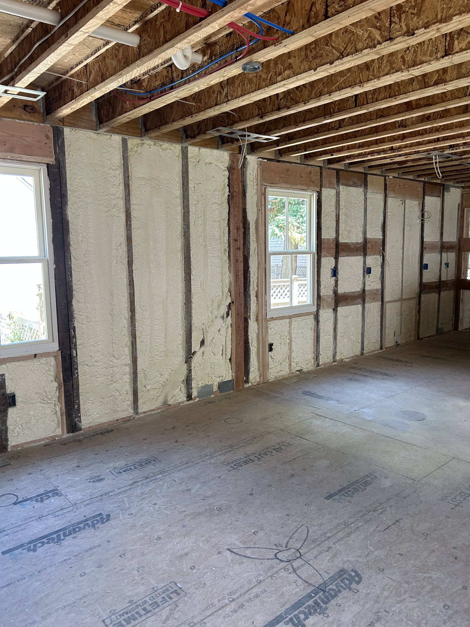 Empty interior room with exposed wooden framing, unfinished walls, and two windows under construction
