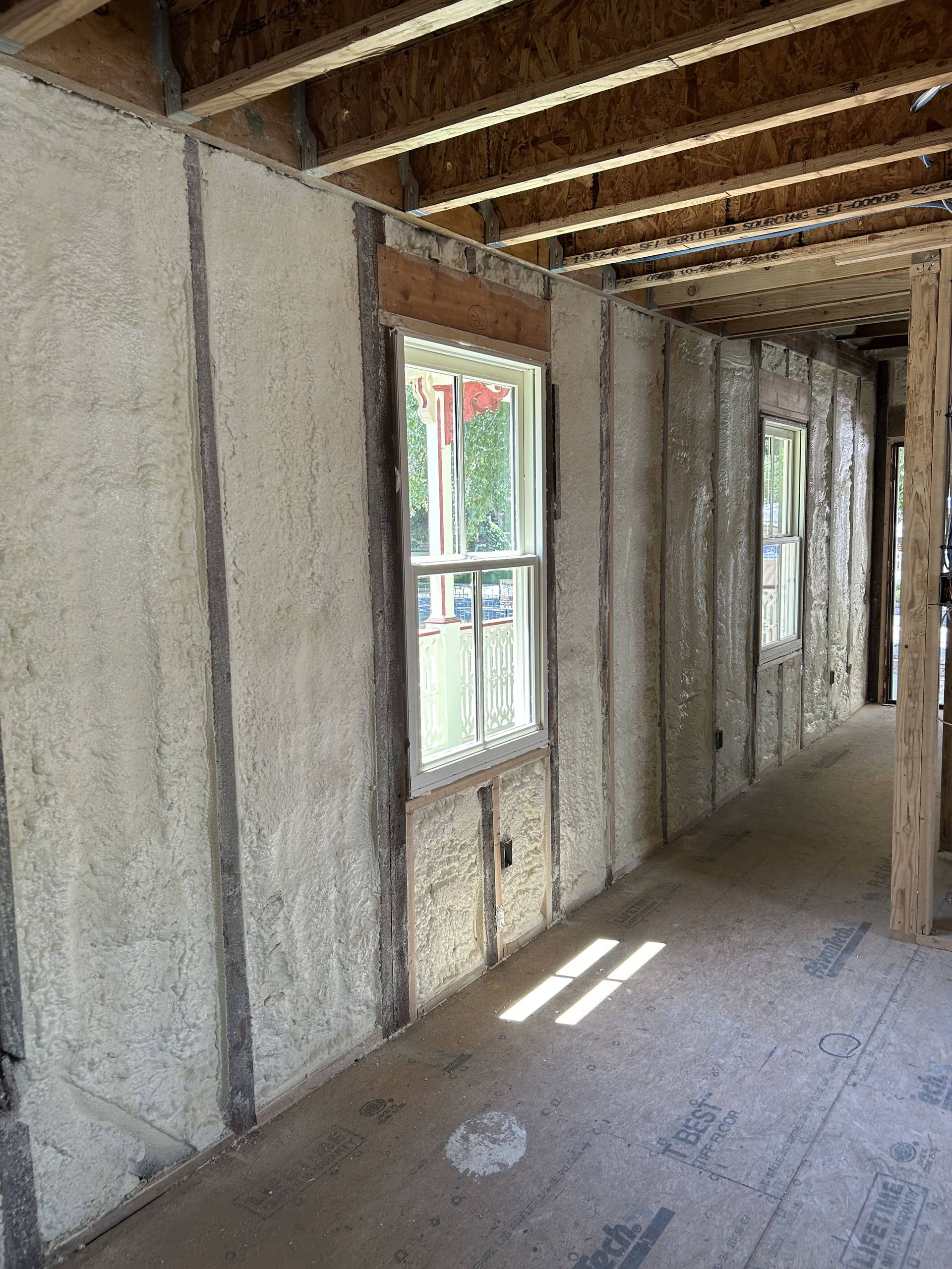 Unfinished interior with insulated walls, exposed beams, and narrow windows casting light on the wooden floor.
