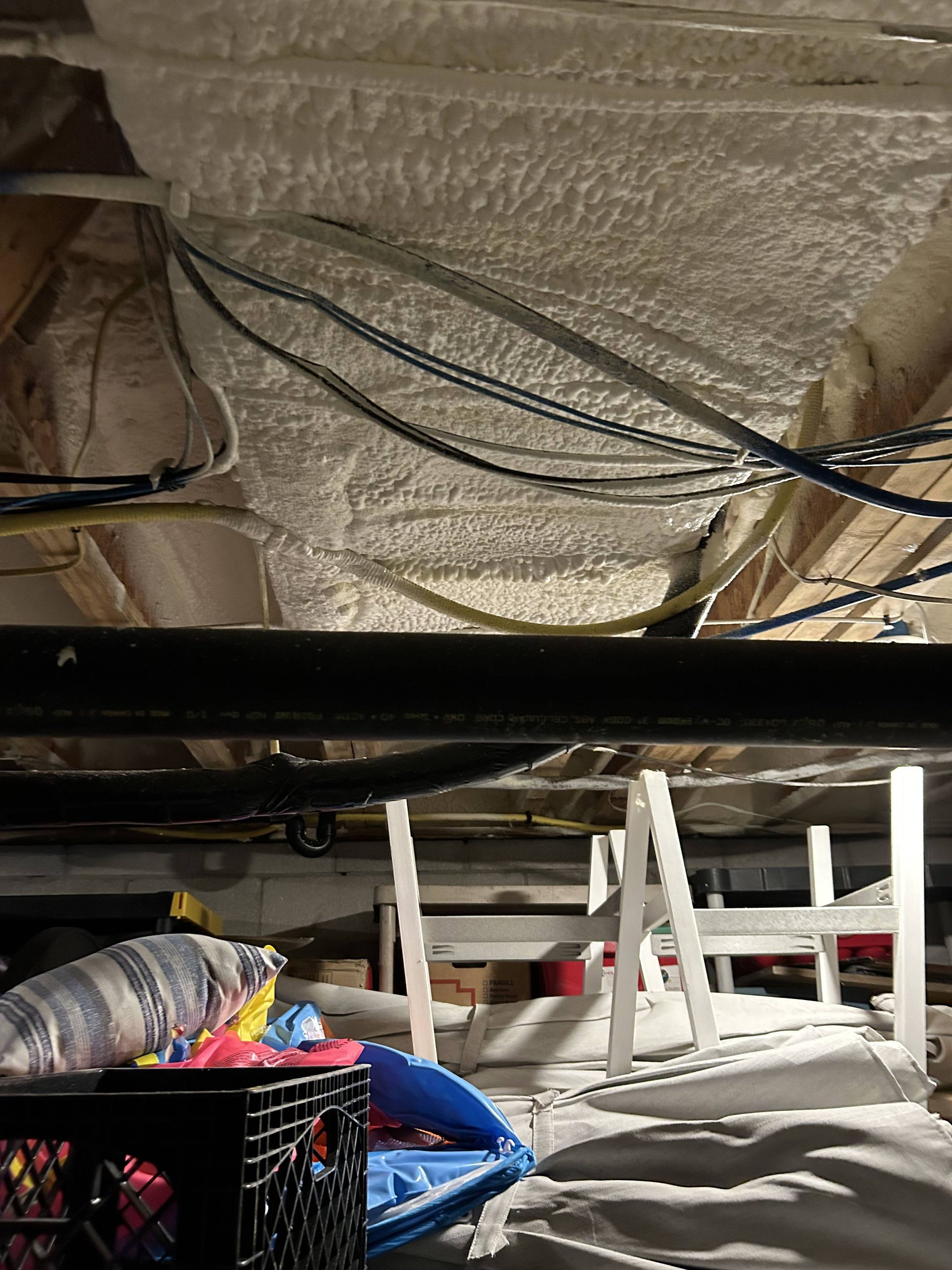 Utility room ceiling with exposed insulation, black cables, and white storage shelves below