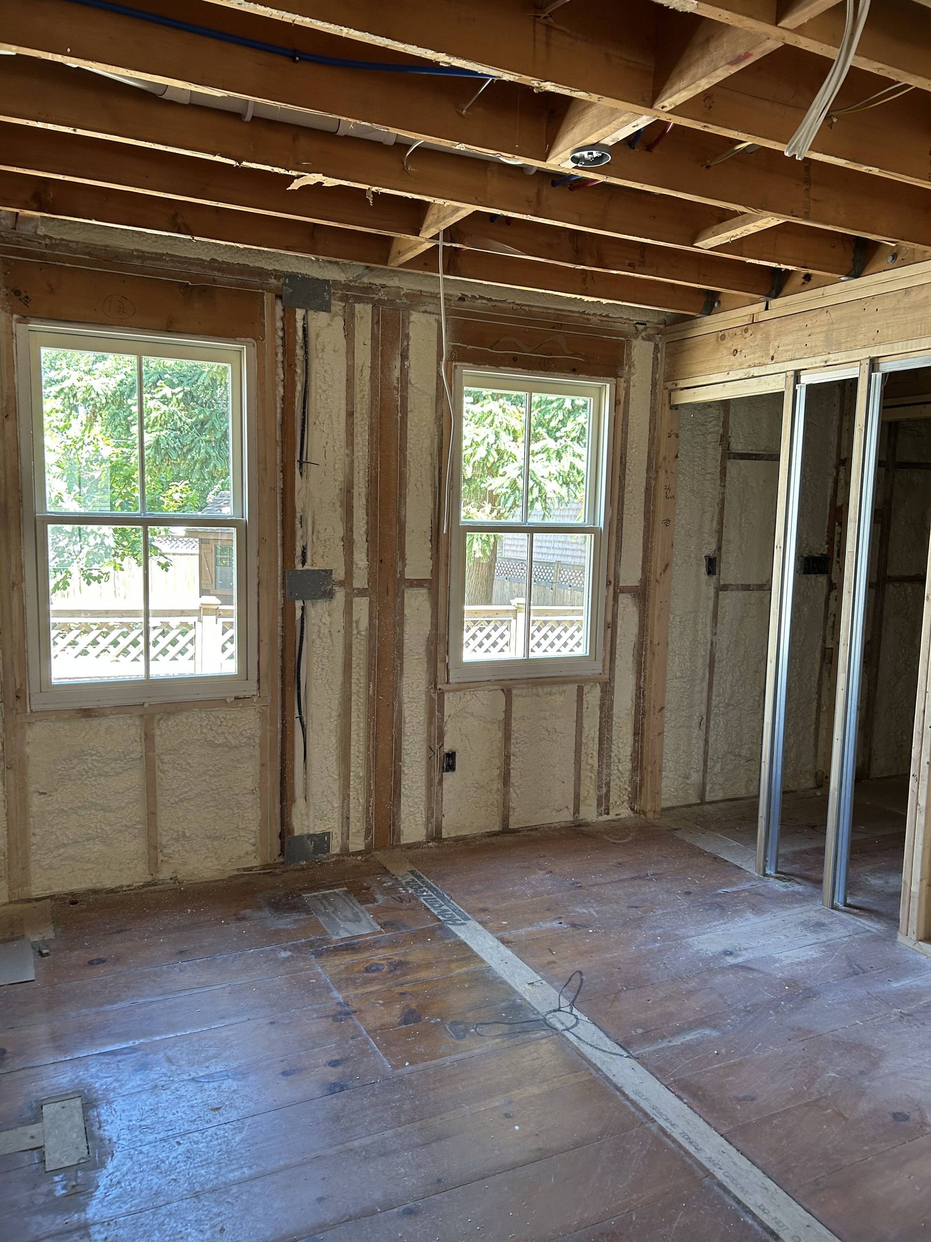 Partially renovated room with exposed framing, insulation, two windows, and unfinished floorboards