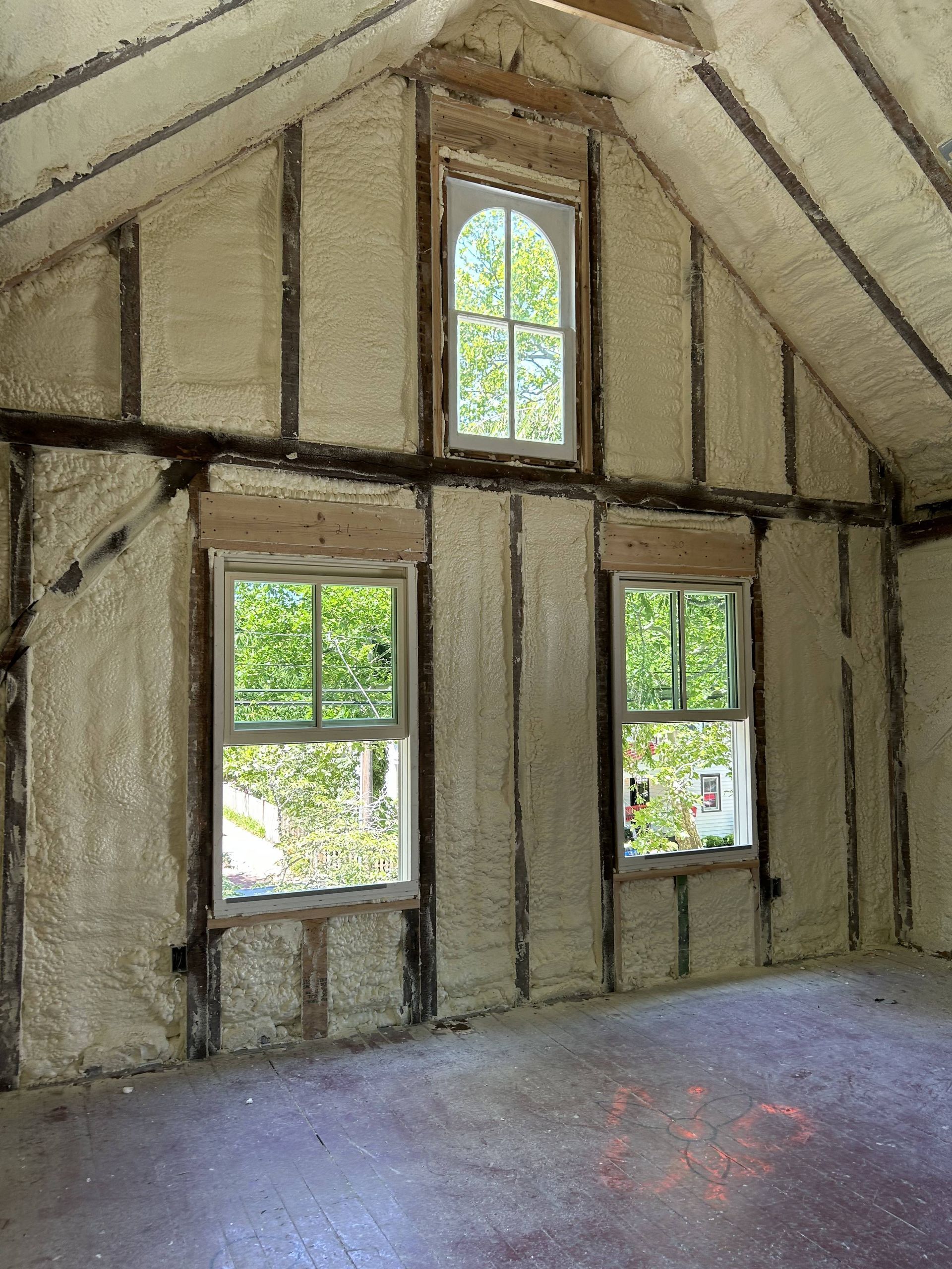 Empty unfinished room with exposed framing and three windows in a sloped ceiling wall.