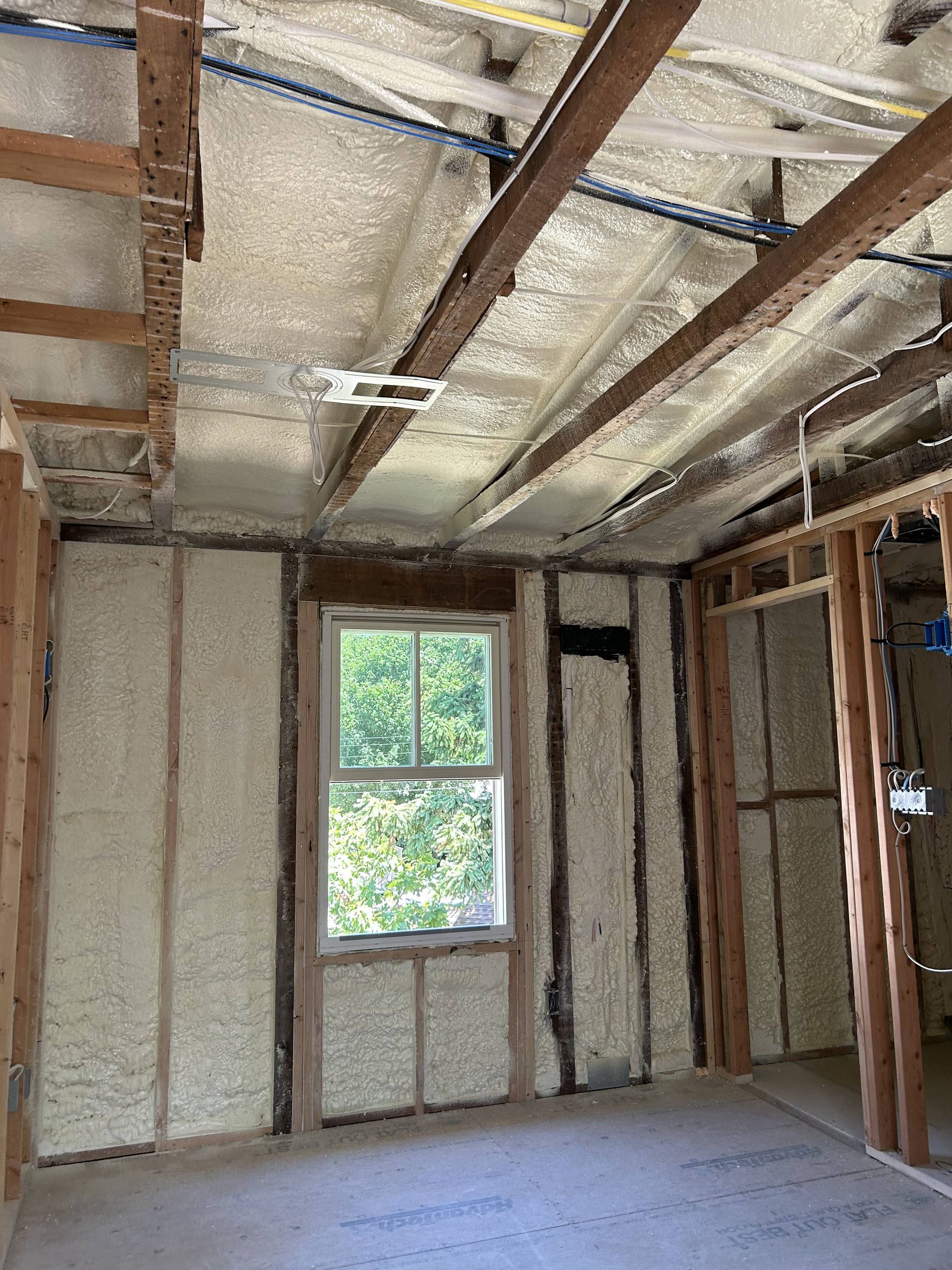 Unfinished room with exposed insulation, beams, and a window letting in daylight.