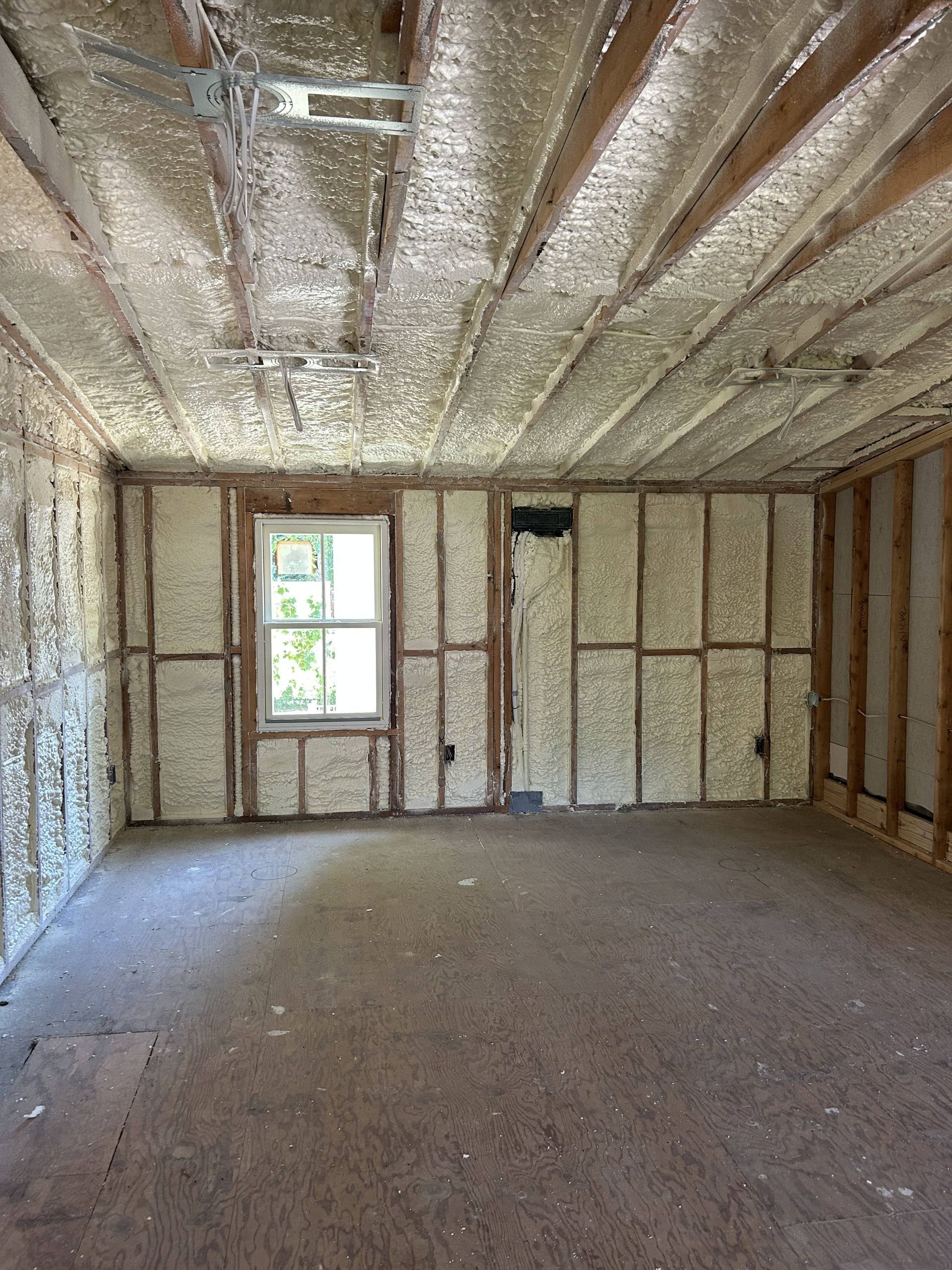 Unfinished insulated room with exposed framing, a small window, and bare subfloor.