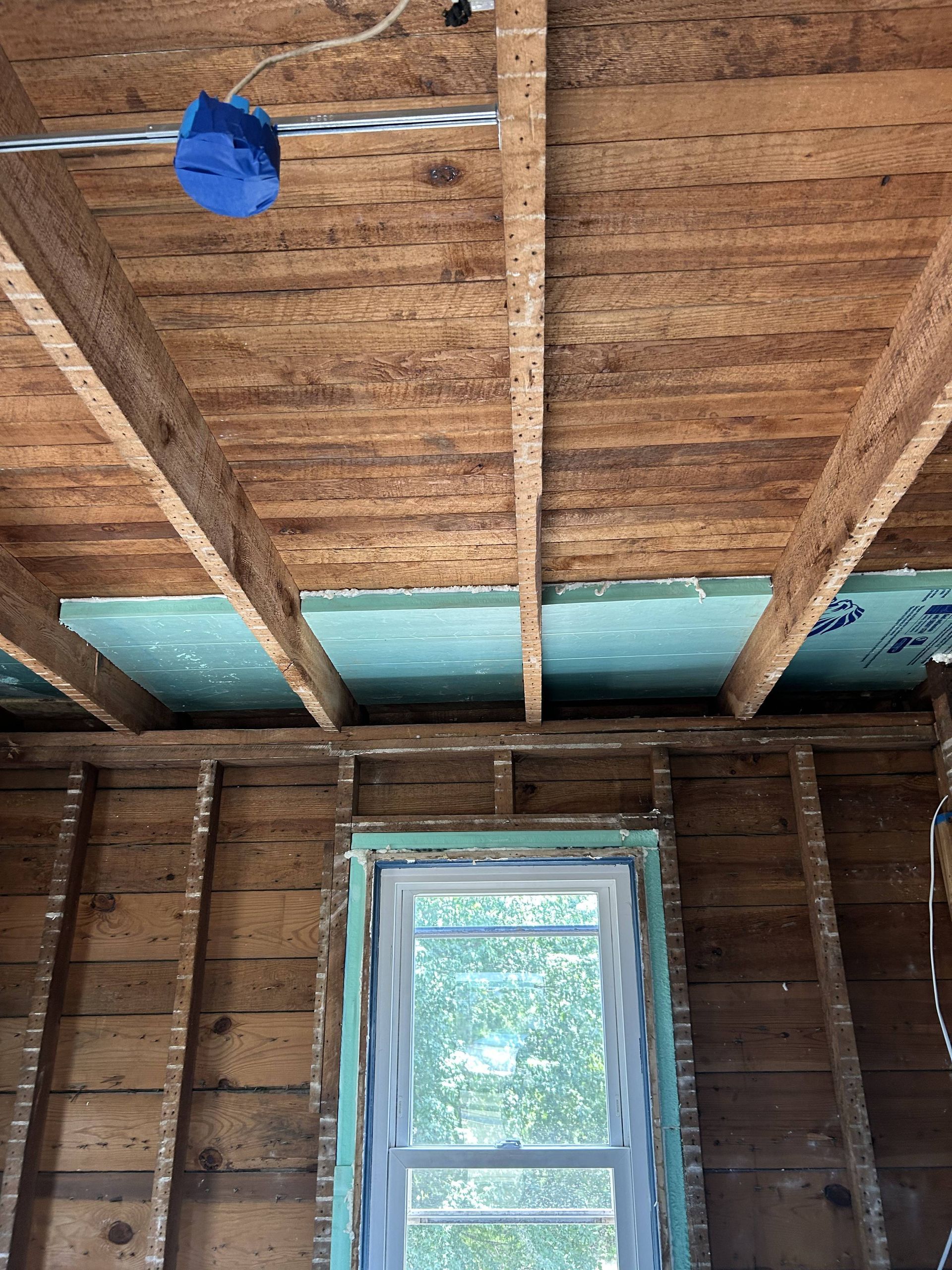 Interior of an unfinished room with exposed wooden rafters and a small window on the back wall.