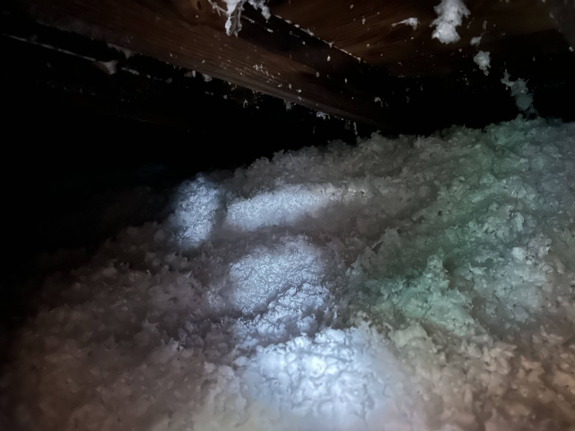 Dim attic crawlspace filled with fluffy white insulation under dark wooden beams