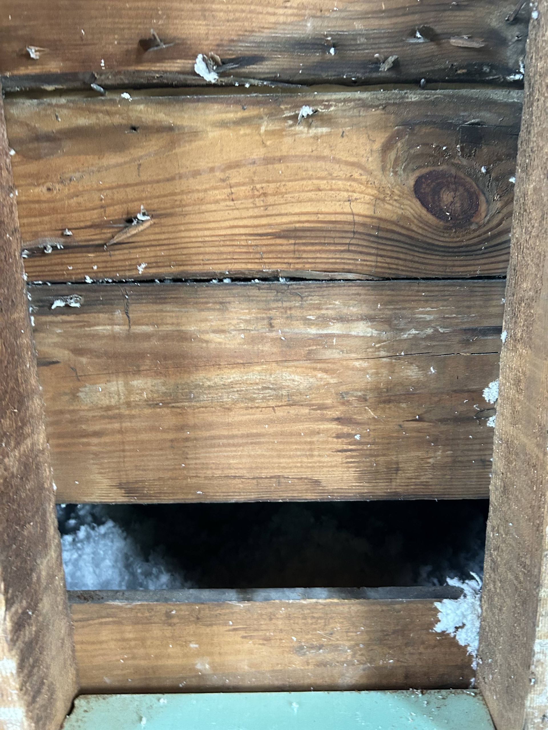 Wooden wall with a rectangular opening and white insulation visible inside