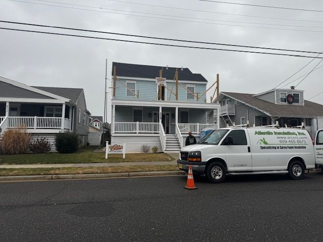 White service van parked in front of a blue house with a damaged roof and two orange cones on the street