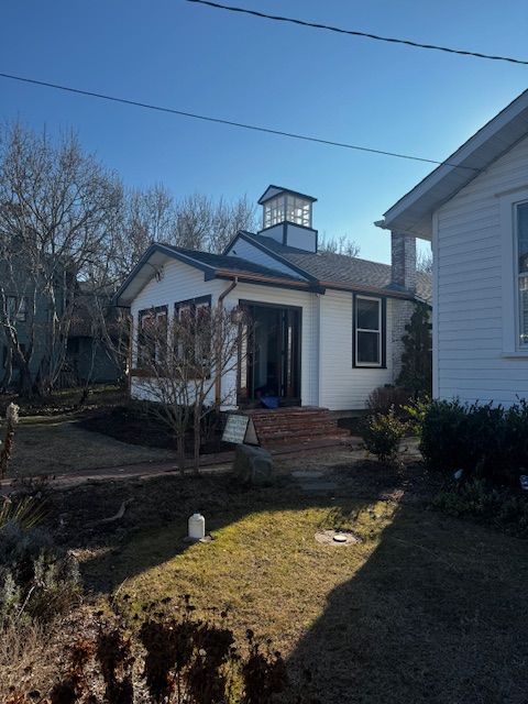 Small white house with a brick porch and cupola, viewed from a grassy front yard on a sunny day