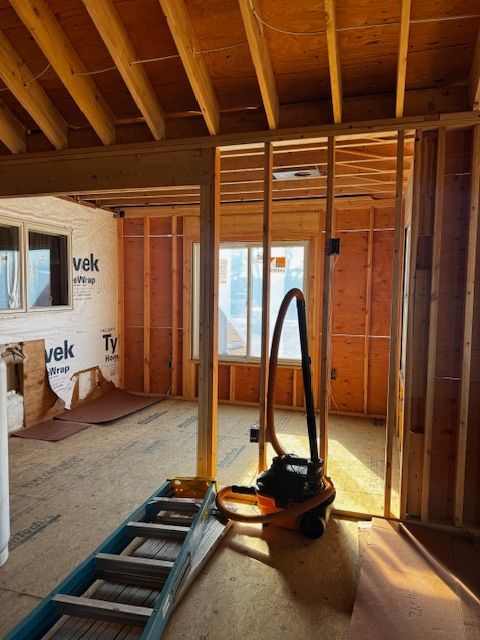 Unfinished room with exposed wood framing, insulation, and a vacuum cleaner on a wooden floor.
