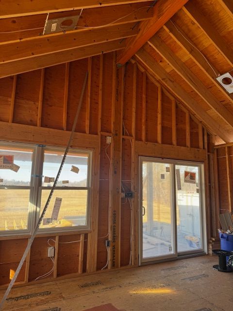 Empty framed room with exposed wood walls, ceiling, and sliding glass doors.