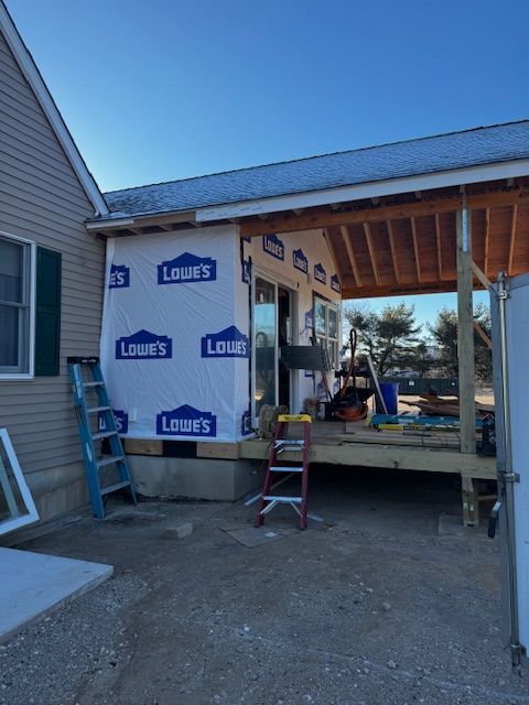 House exterior under construction with Tyvek wrap, ladder, and tools beside a covered porch