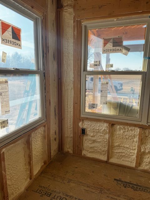 Insulated unfinished corner room with two windows overlooking rooftops and sky
