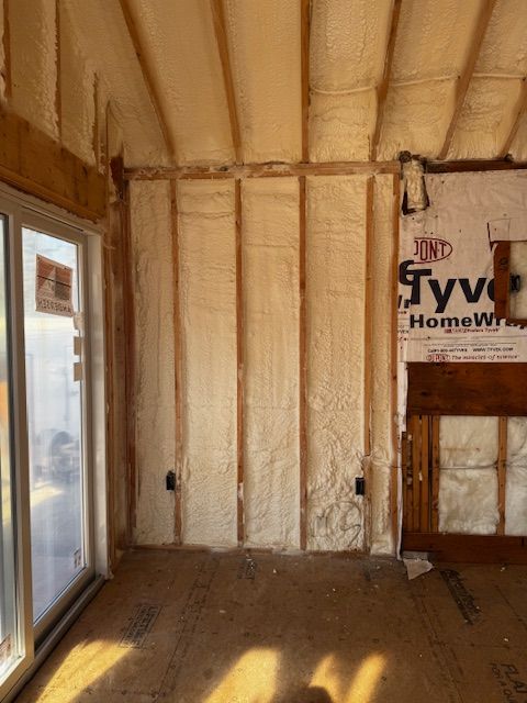 Insulated room under construction with windows, exposed studs, and Tyvek house wrap visible on the wall