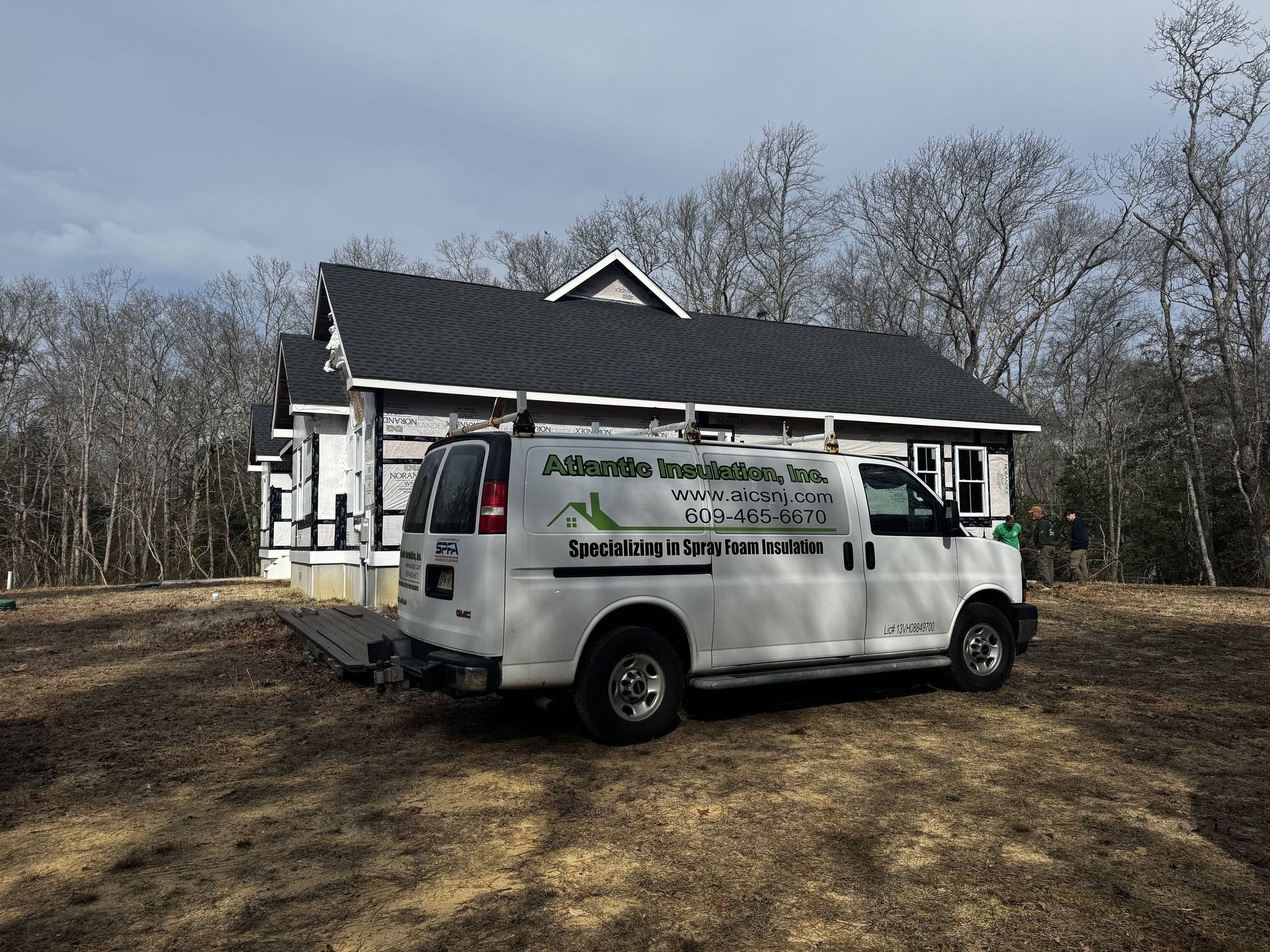 White utility van parked on a dirt lot beside a small building under bare trees.