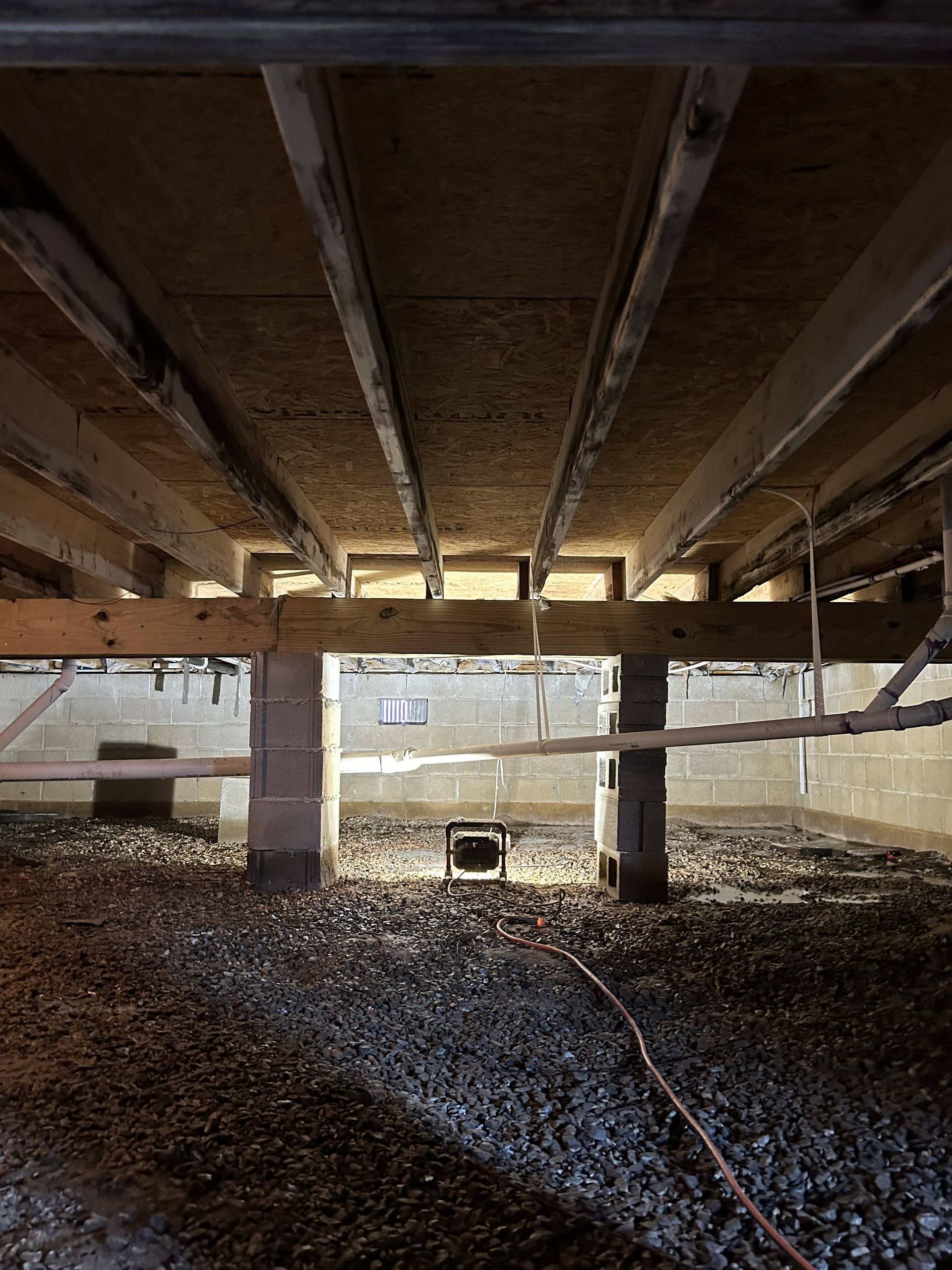 Under a concrete structure, a gravel-covered floor with a hose and bright light in the distance
