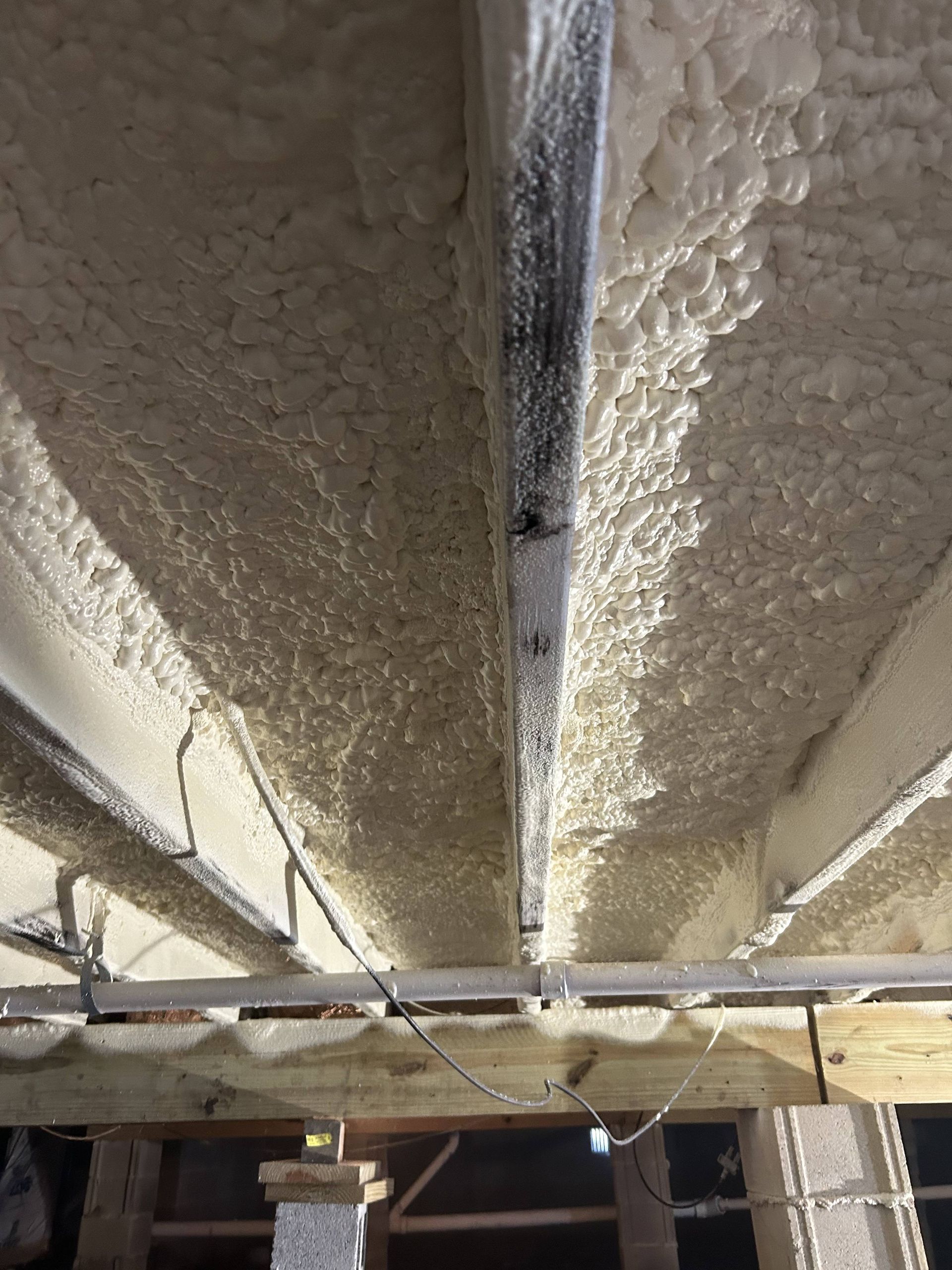 Construction site ceiling with spray foam insulation and exposed beams above a scaffolding frame