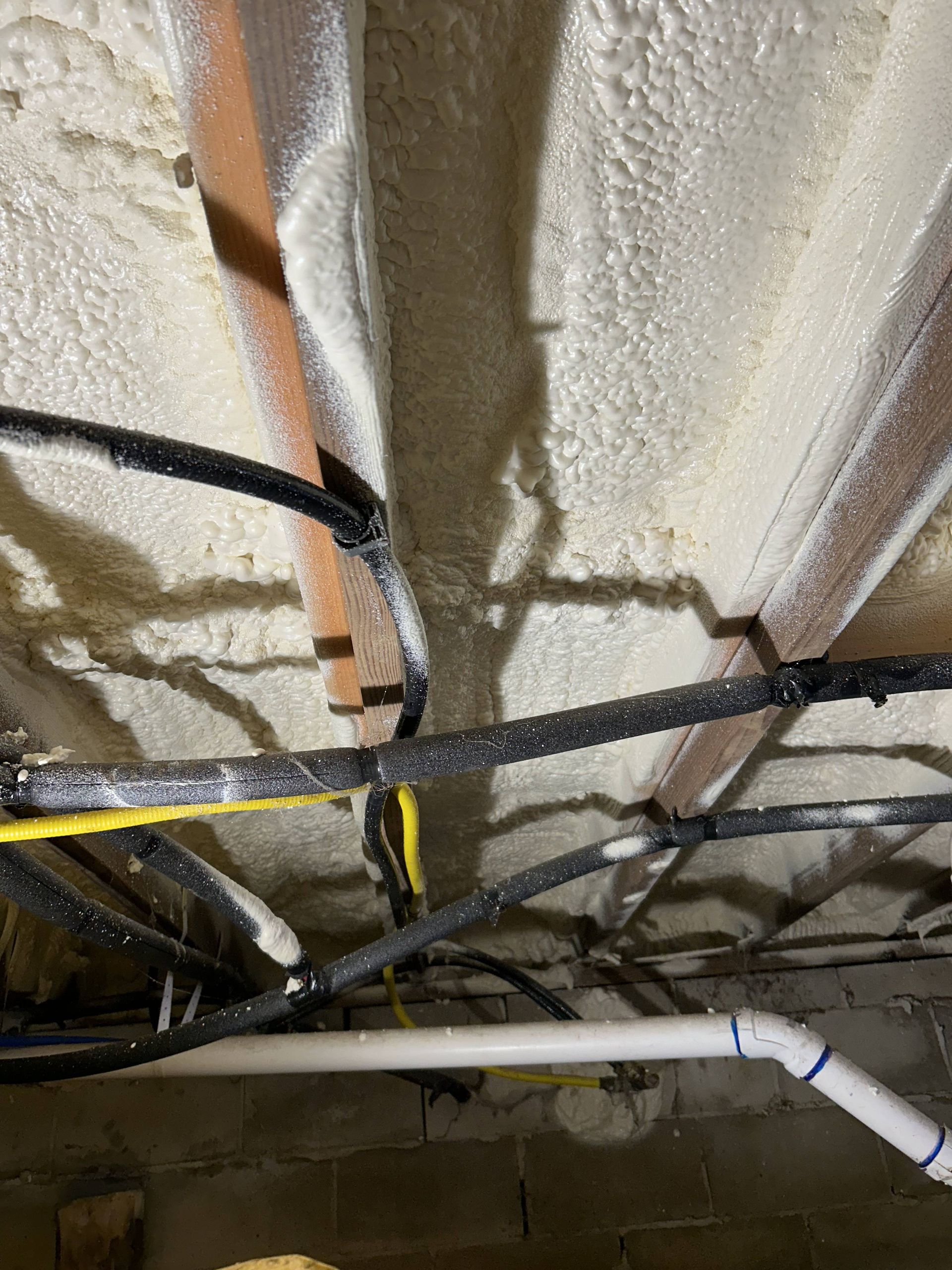 Foam-insulated ceiling with exposed black cables and a white pipe in a utility space