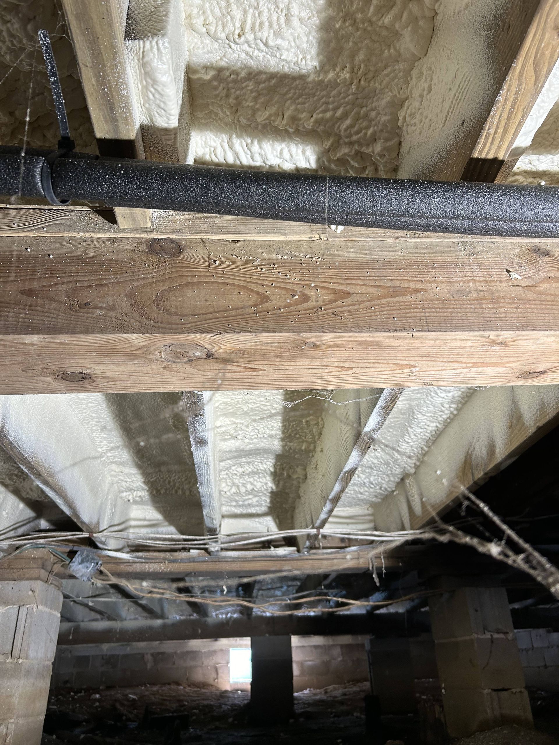 Insulated crawlspace with exposed wooden beams, ducting, and concrete foundation supports.