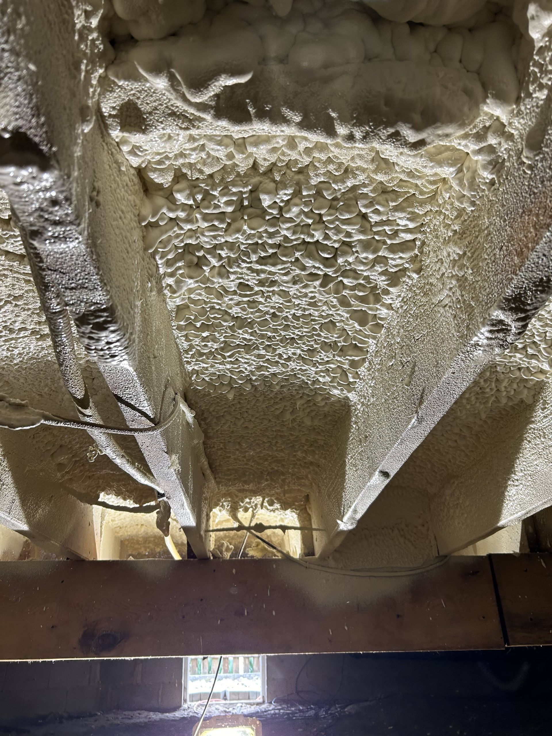 Exposed attic insulation and wooden beams, with a small window below.
