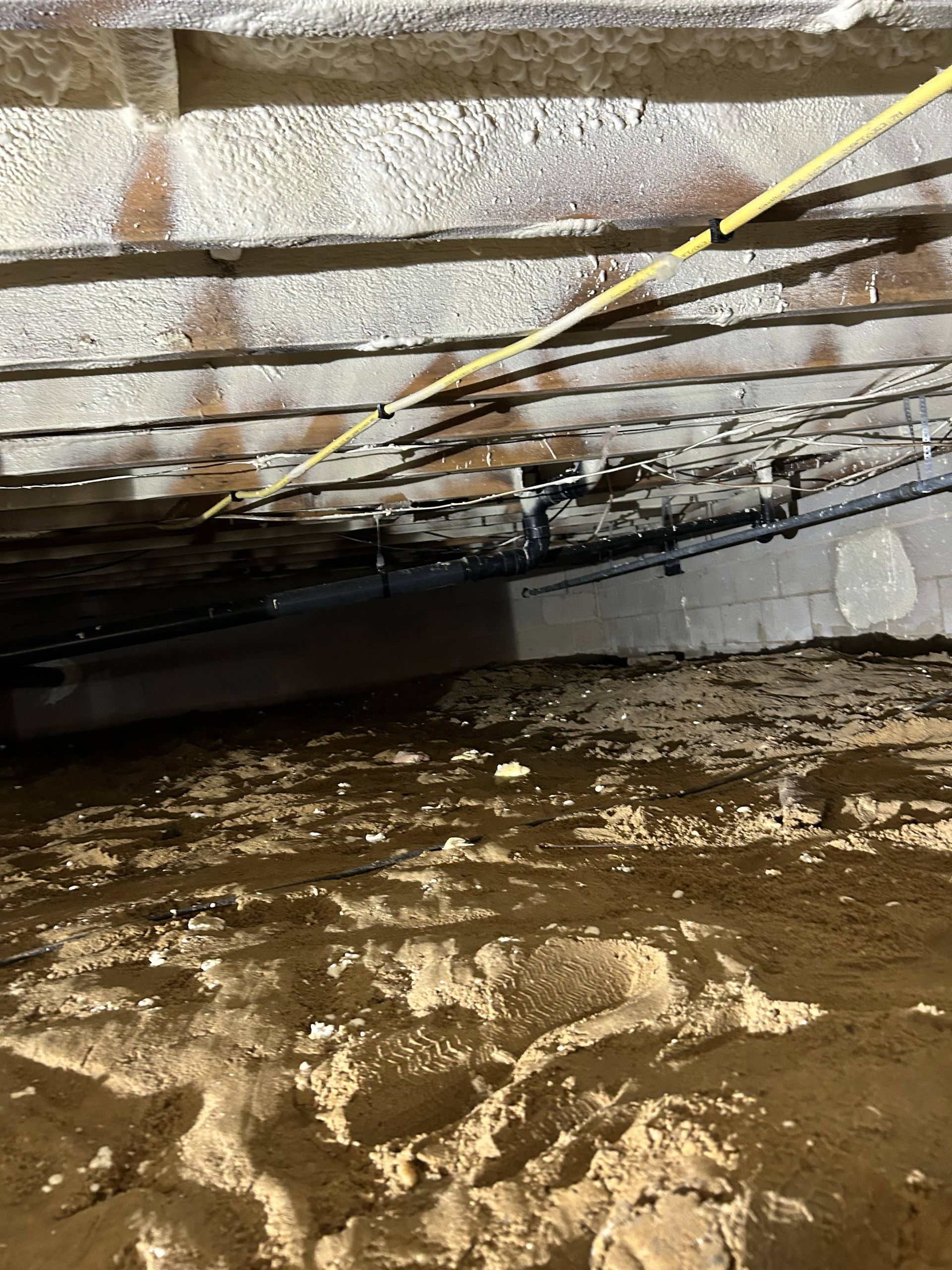 Crawlspace under a house with exposed beams, insulation, and a muddy floor with standing water