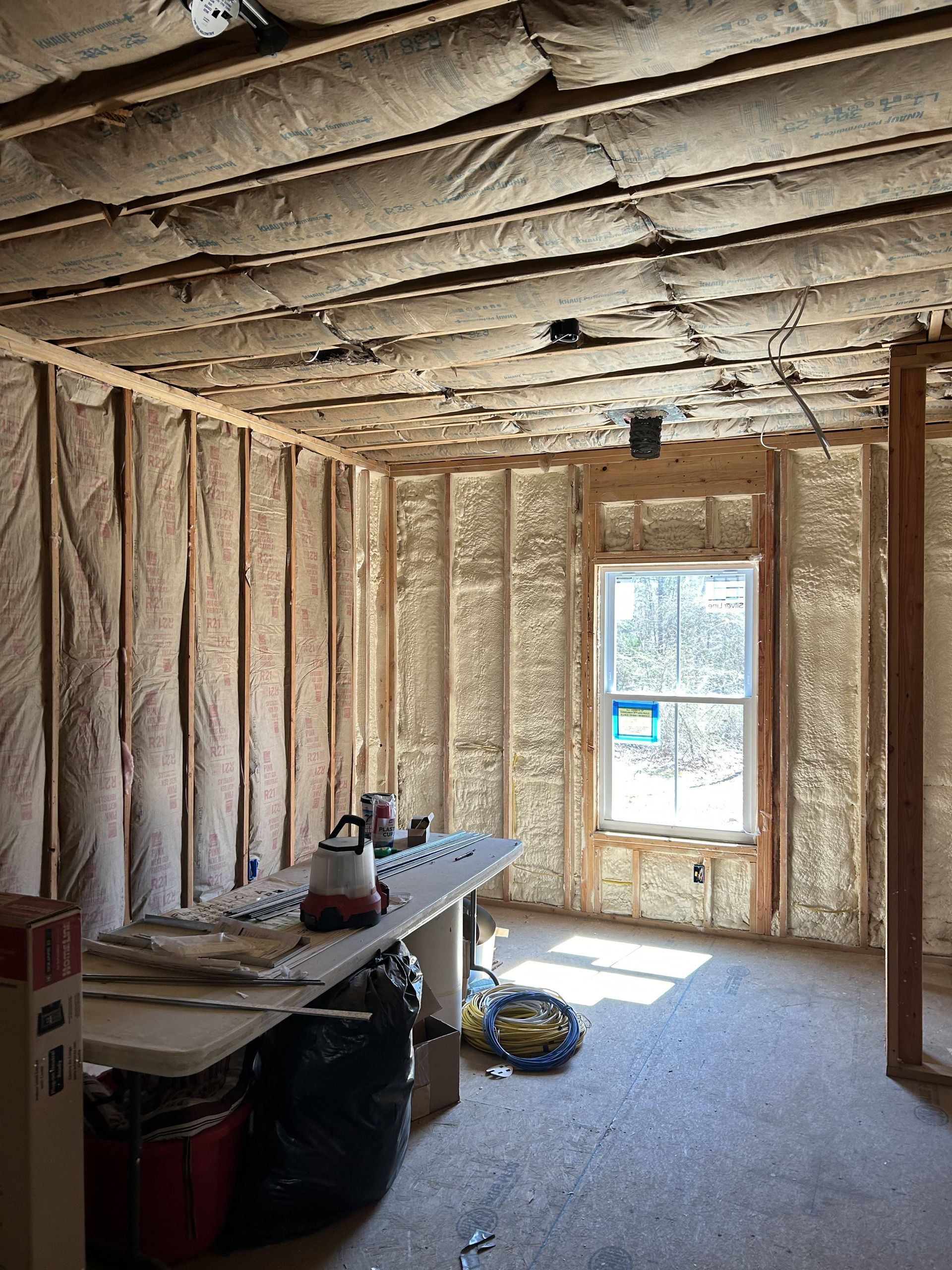 Insulated unfinished room with exposed studs, a window, workbench, and construction materials on the floor