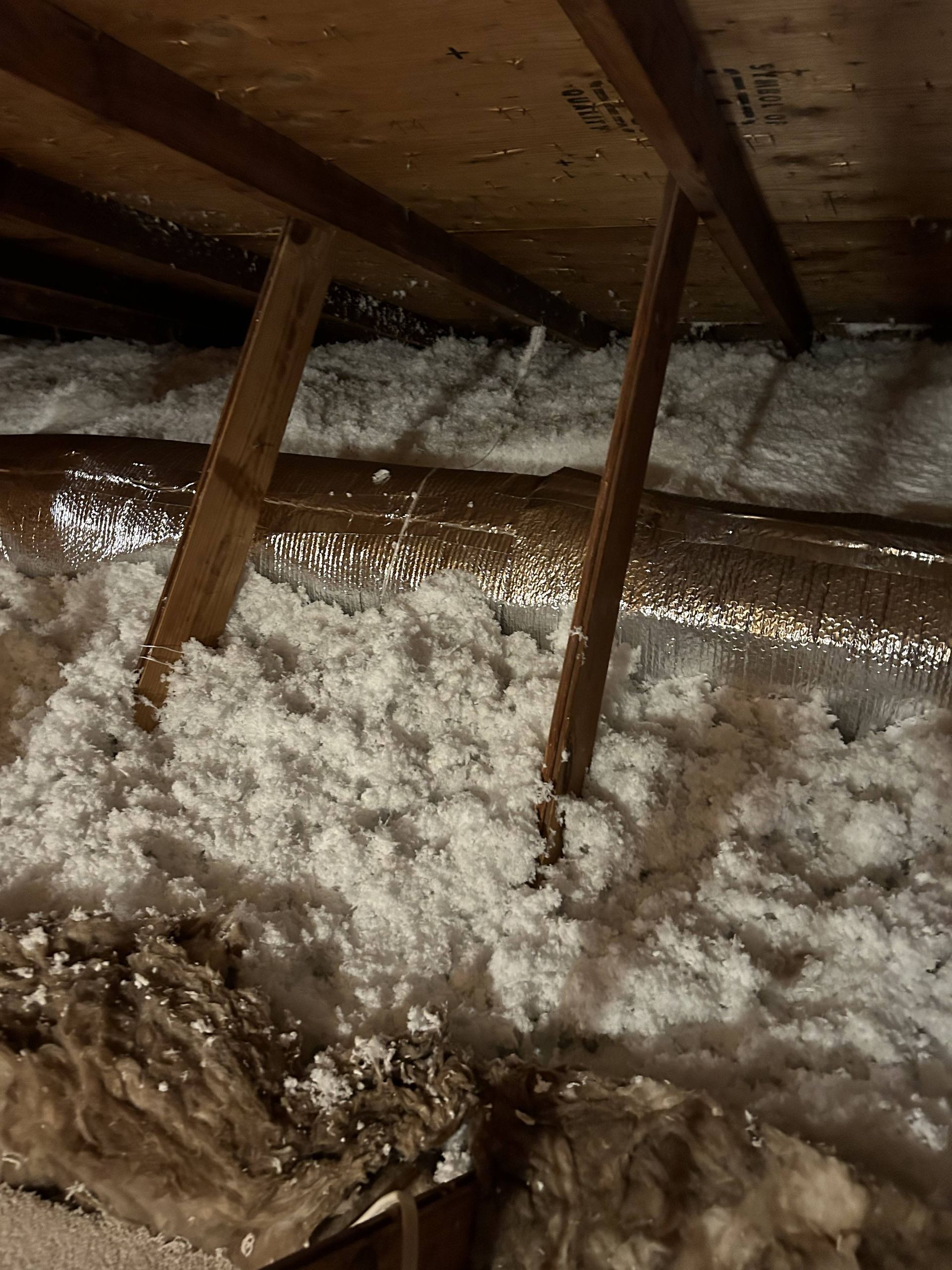 Attic with blown-in white insulation and exposed wooden rafters.