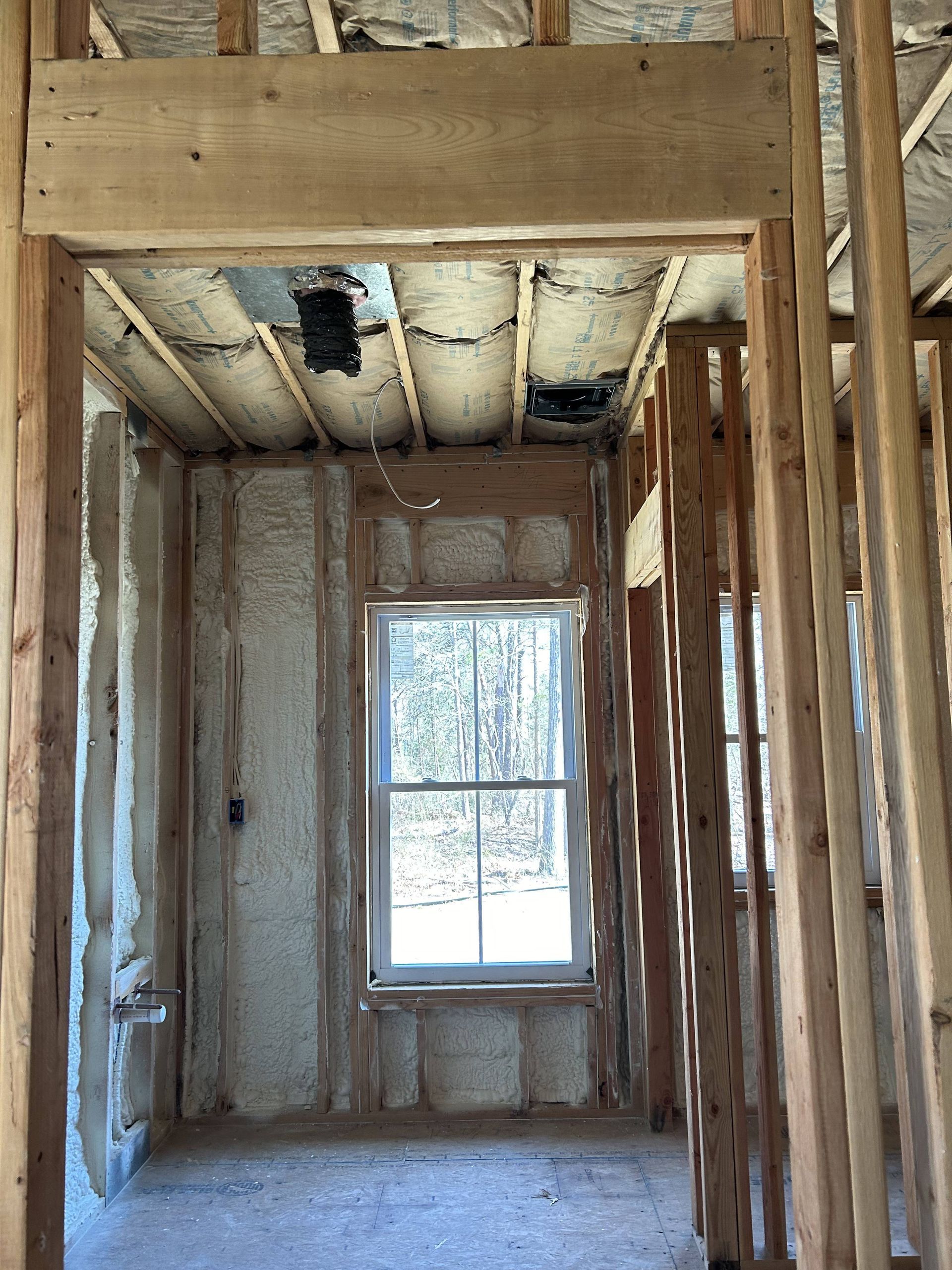 Unfinished interior wall framing with a centered window and exposed ceiling insulation.