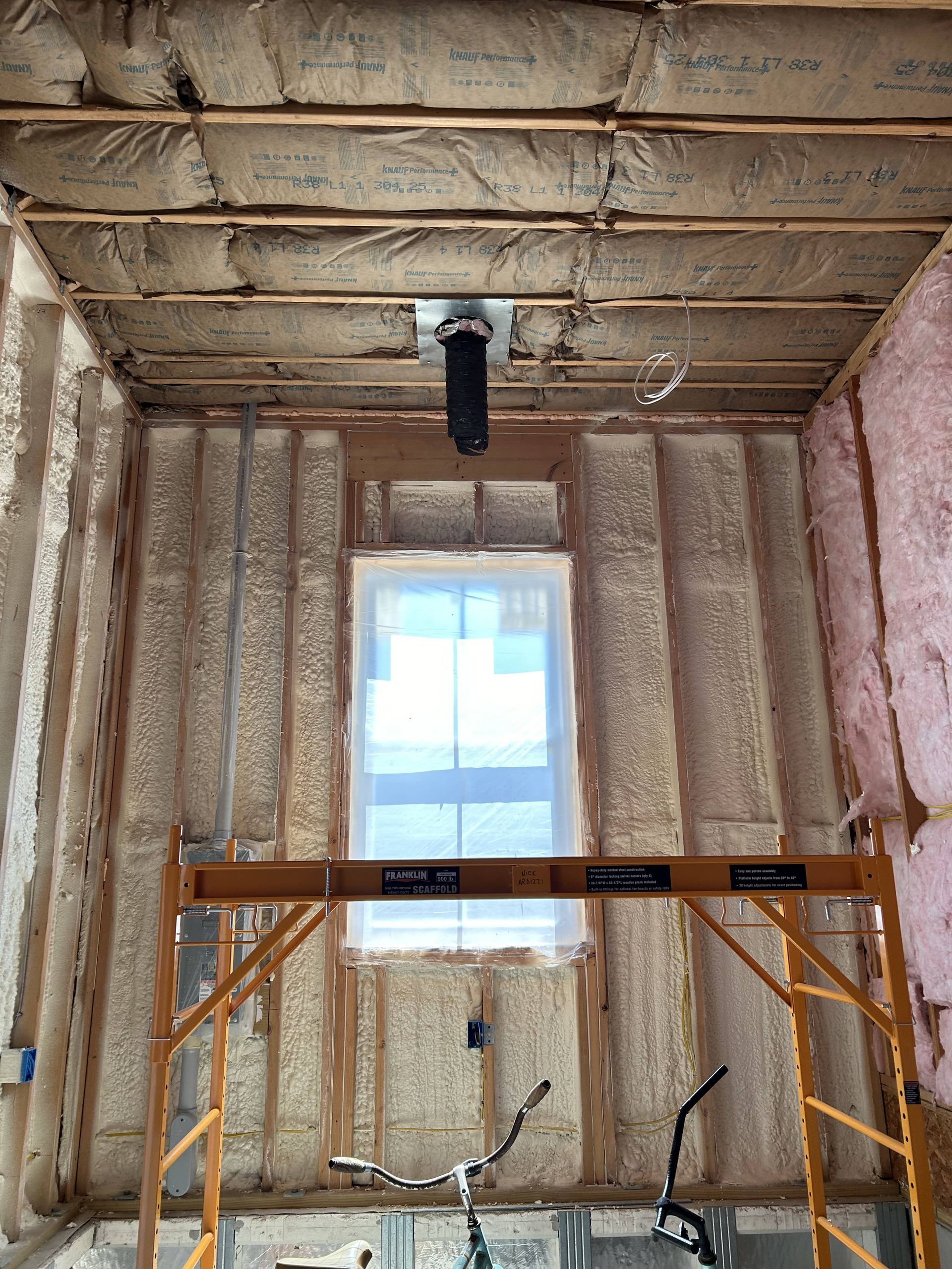 Partially insulated room with a window, scaffold, and exposed ceiling during renovation