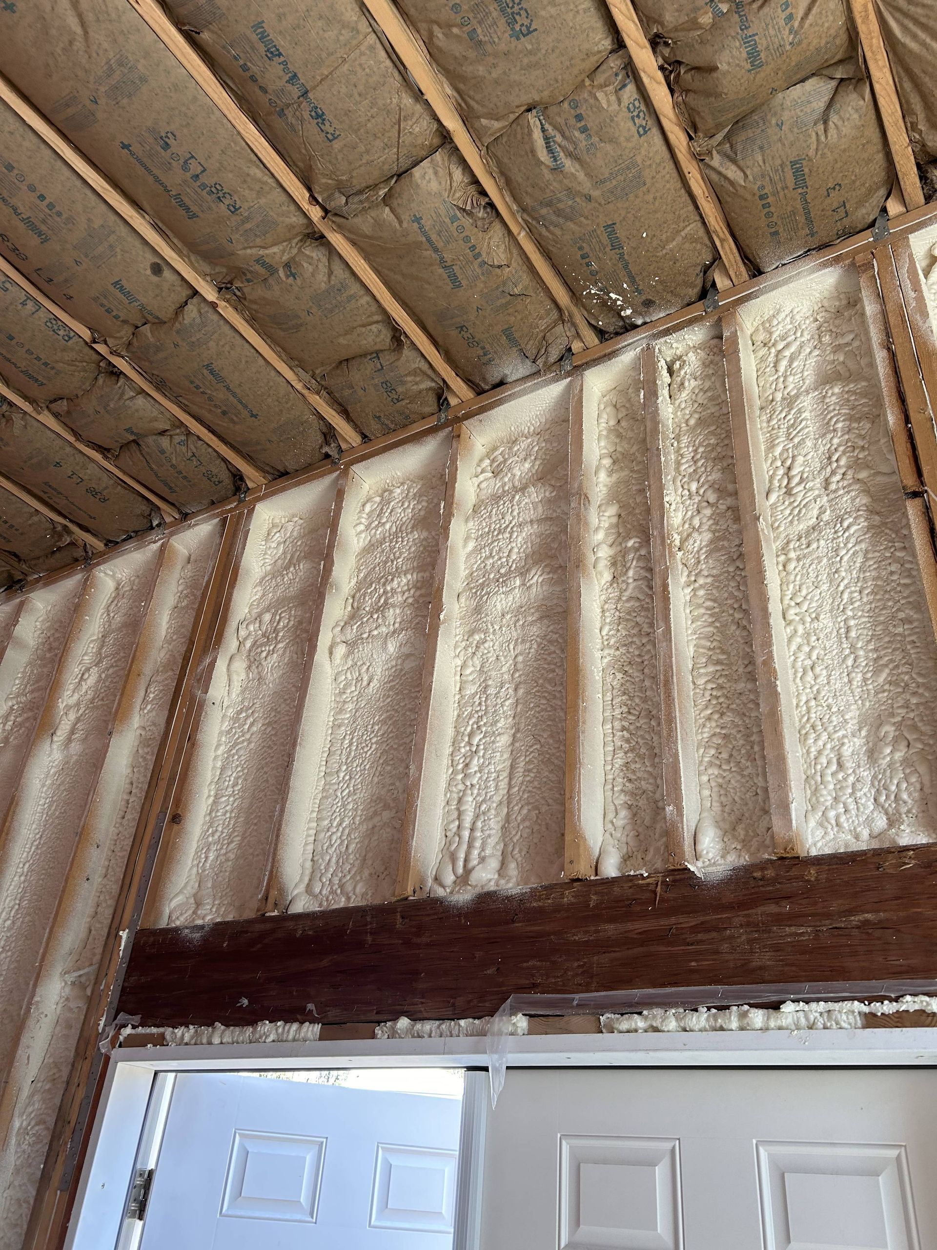 Close-up of an unfinished wall and ceiling with exposed insulation above white double doors