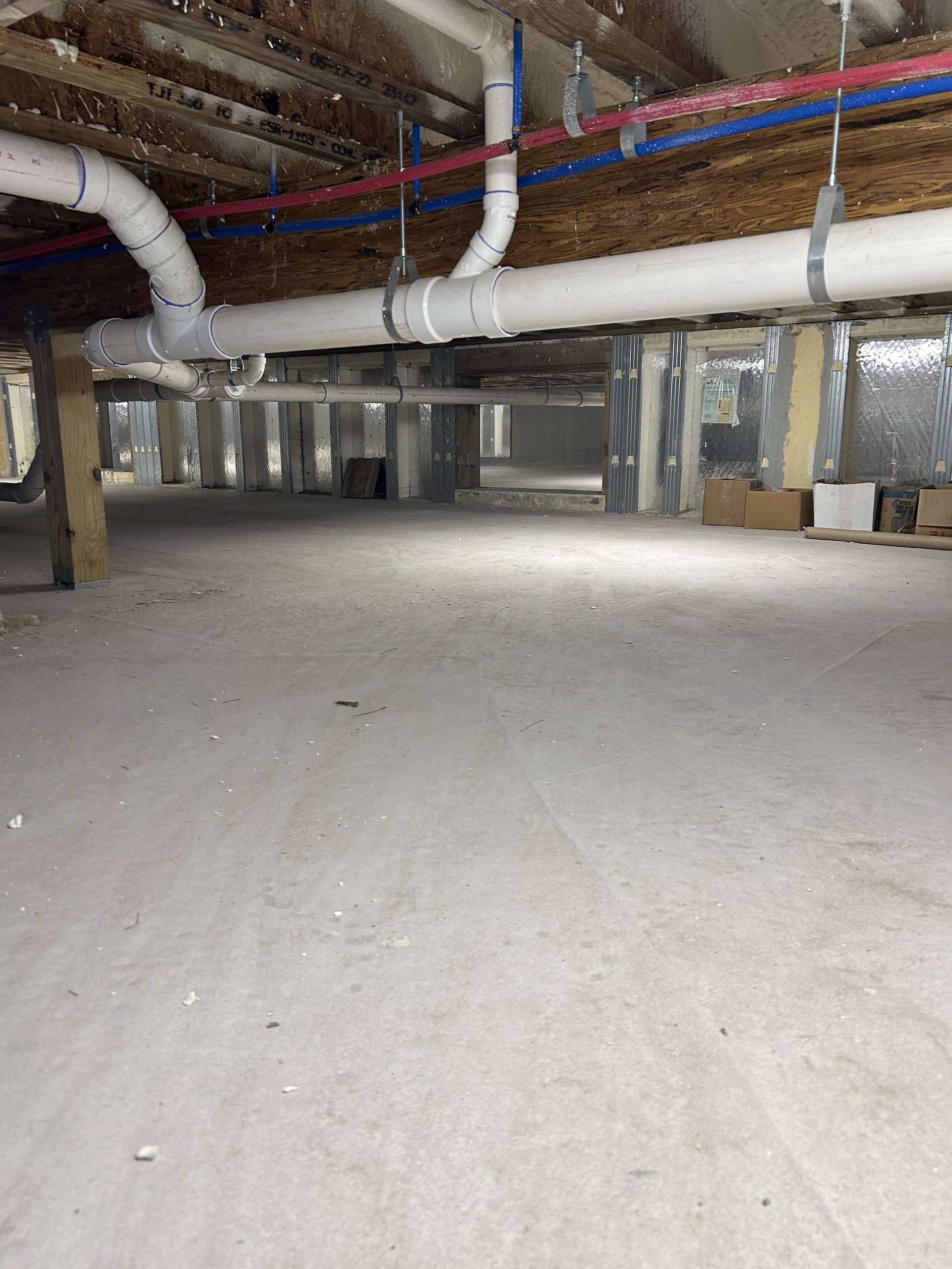 Low crawlspace with exposed pipes, ducts, and concrete floor underneath a building.