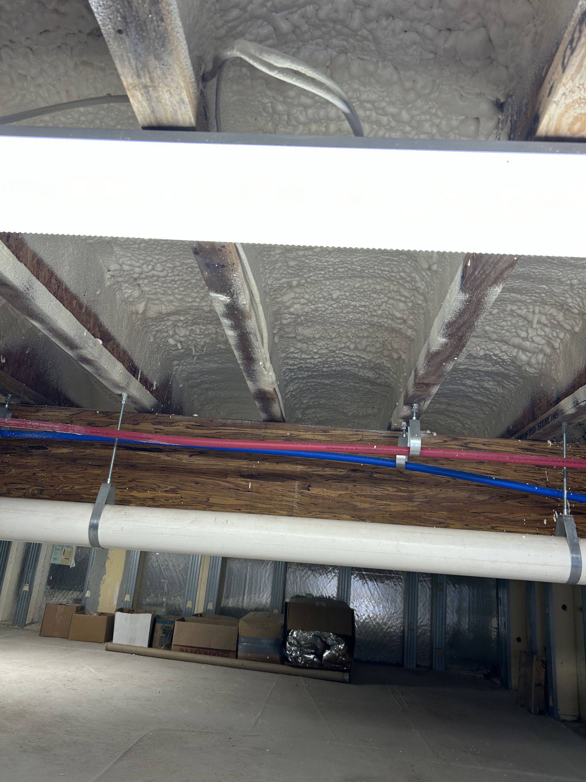 Dim industrial ceiling with exposed beams, pipes, and insulation in a basement or utility space