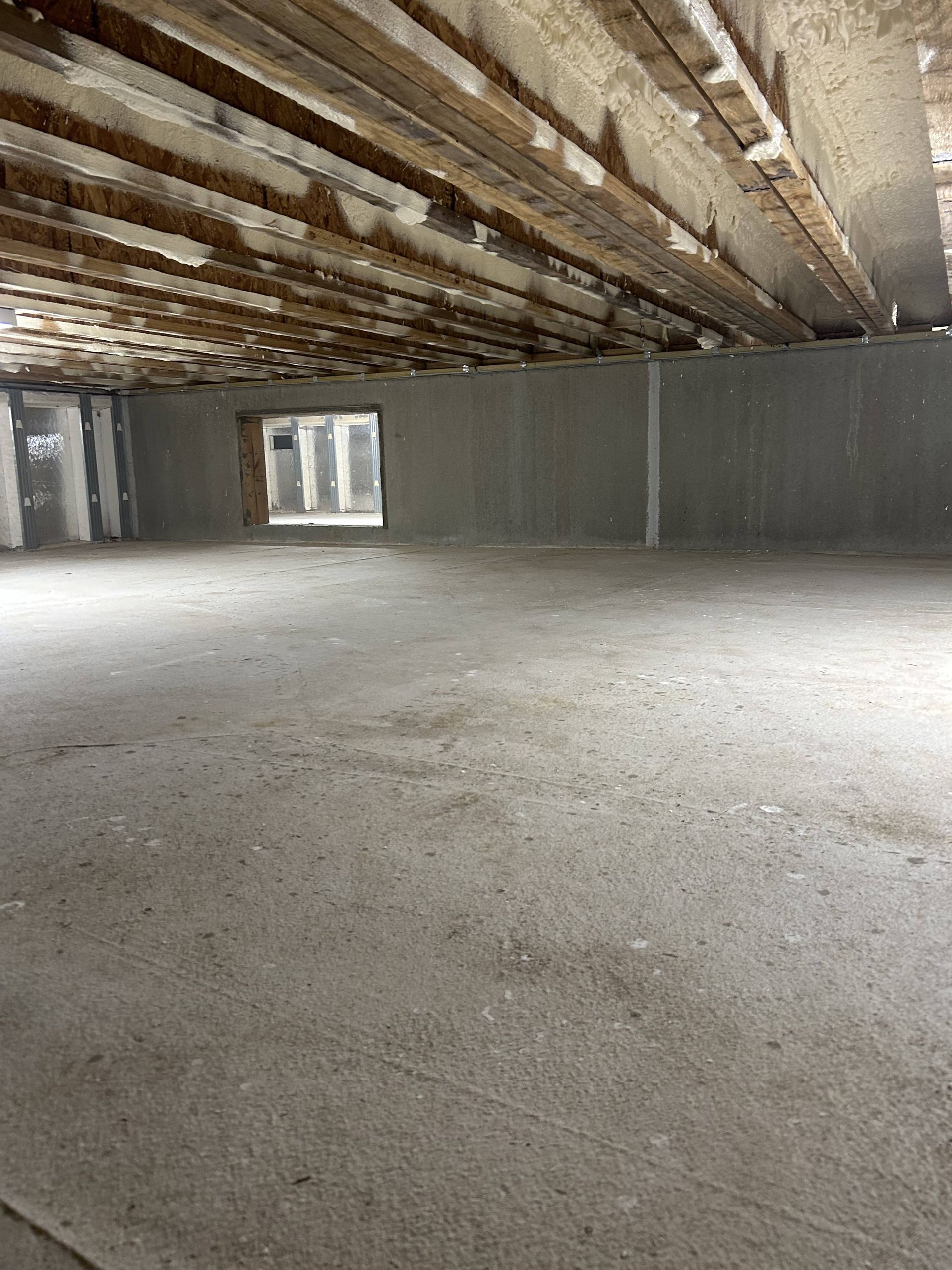 Empty unfinished concrete room with exposed beams and a window at the far end