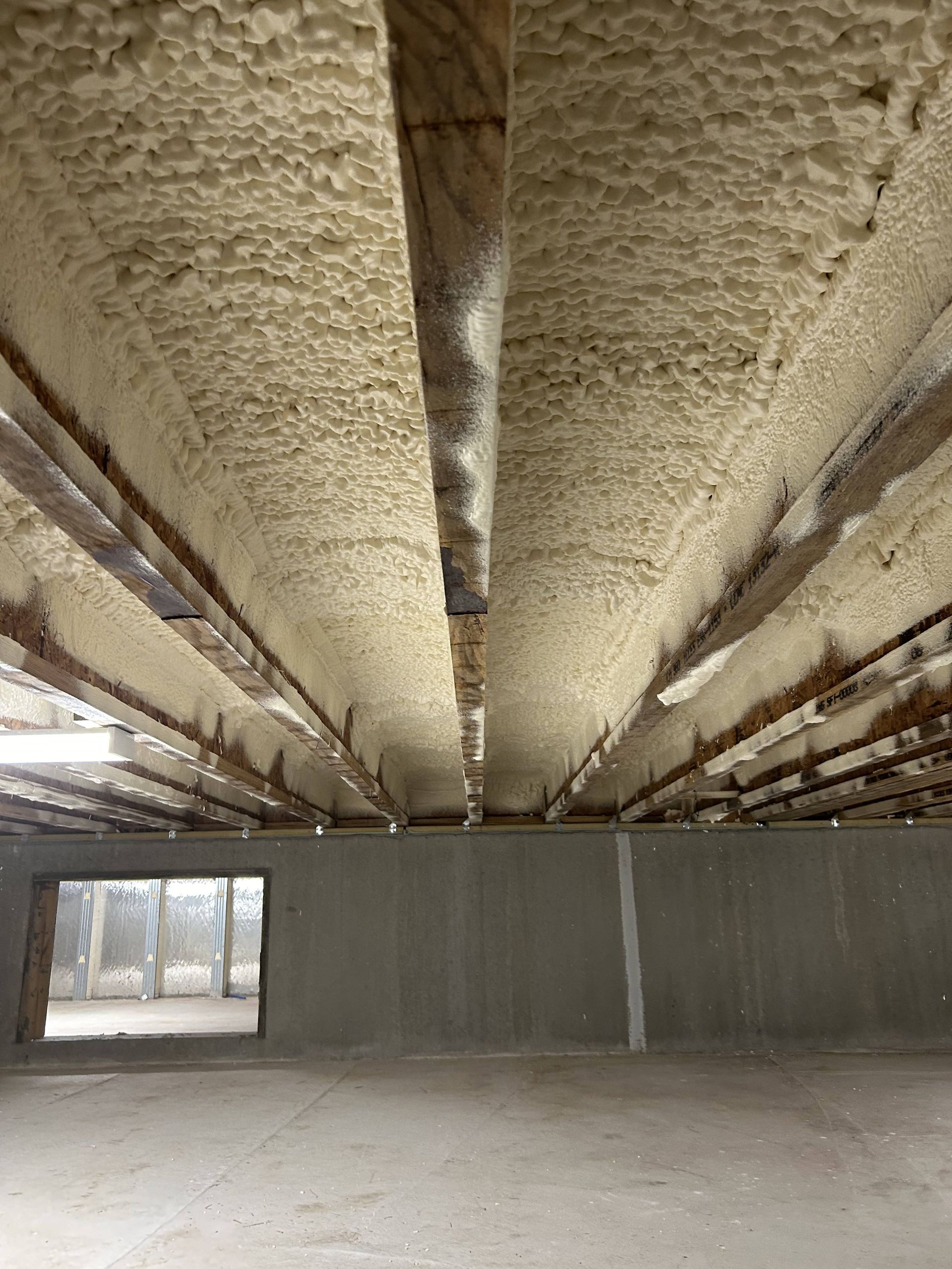 Empty unfinished basement with spray-foam insulated ceiling and concrete floor.