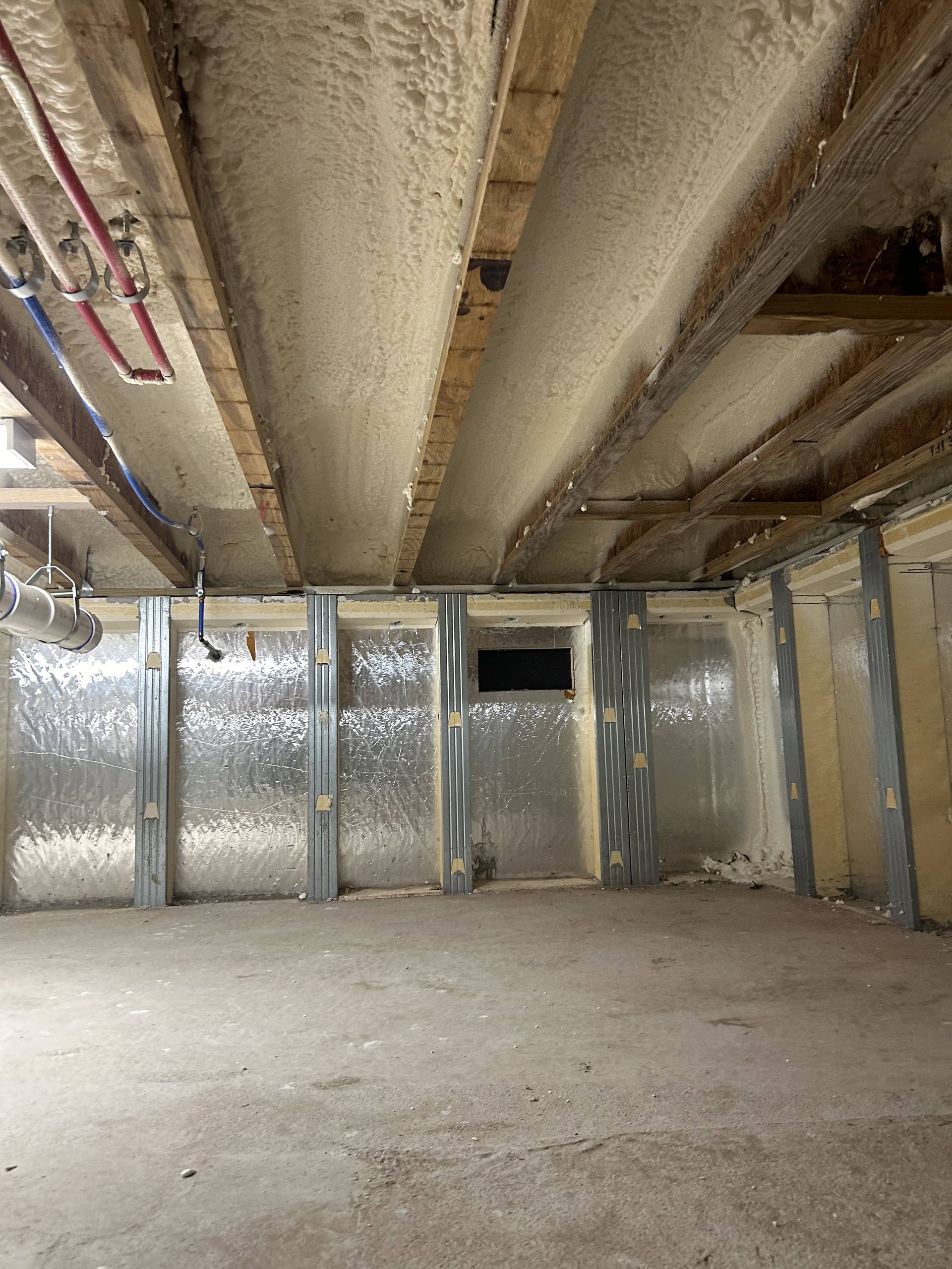 Empty unfinished basement with exposed insulation, concrete floor, and ceiling joists