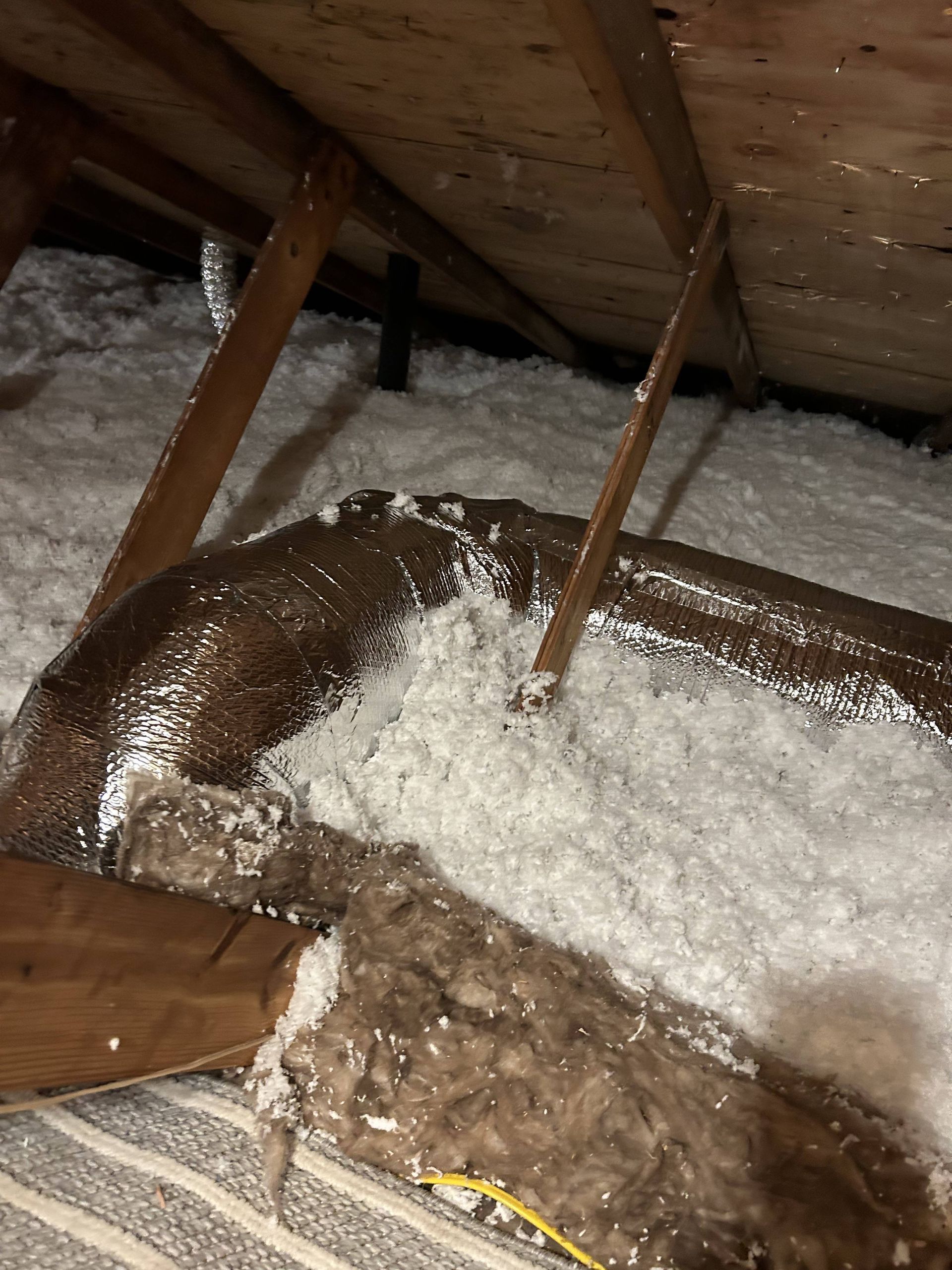 Attic insulation piled around wooden rafters and a roof beam with snow or frost on top
