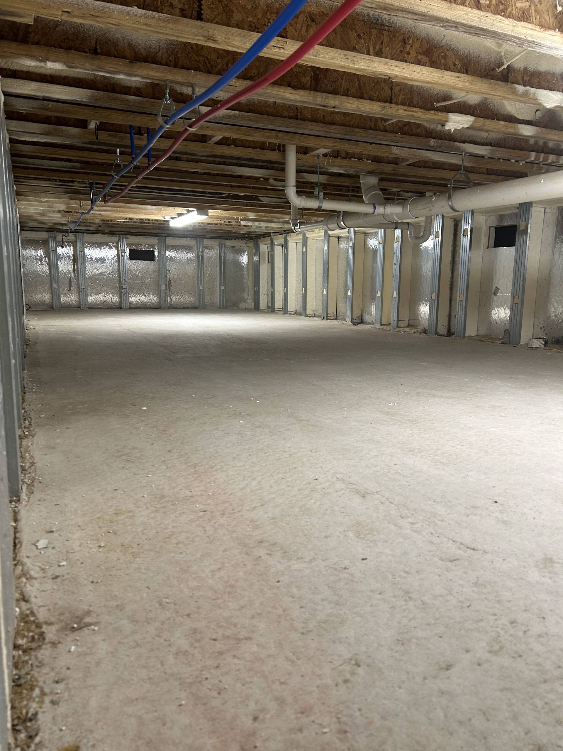 Unfinished basement with exposed joists, support columns, and rough concrete floor.