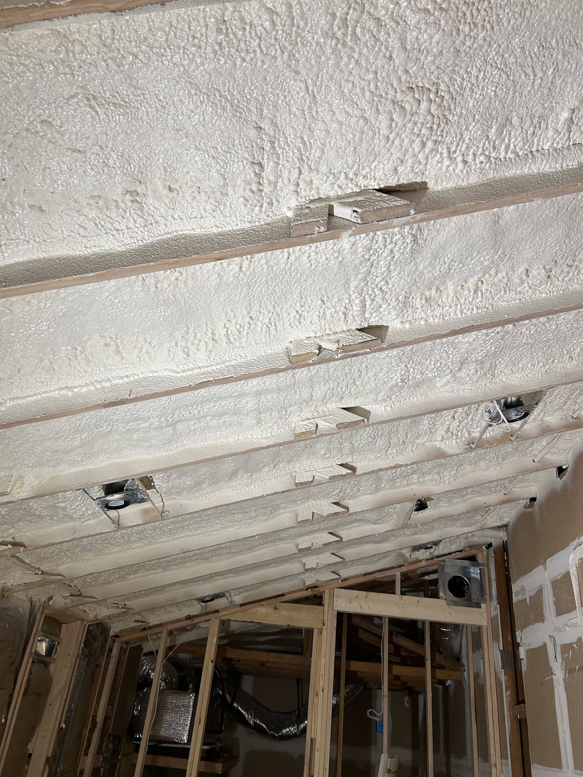 Damaged unfinished ceiling with exposed insulation, wood framing, and visible holes in a room under construction