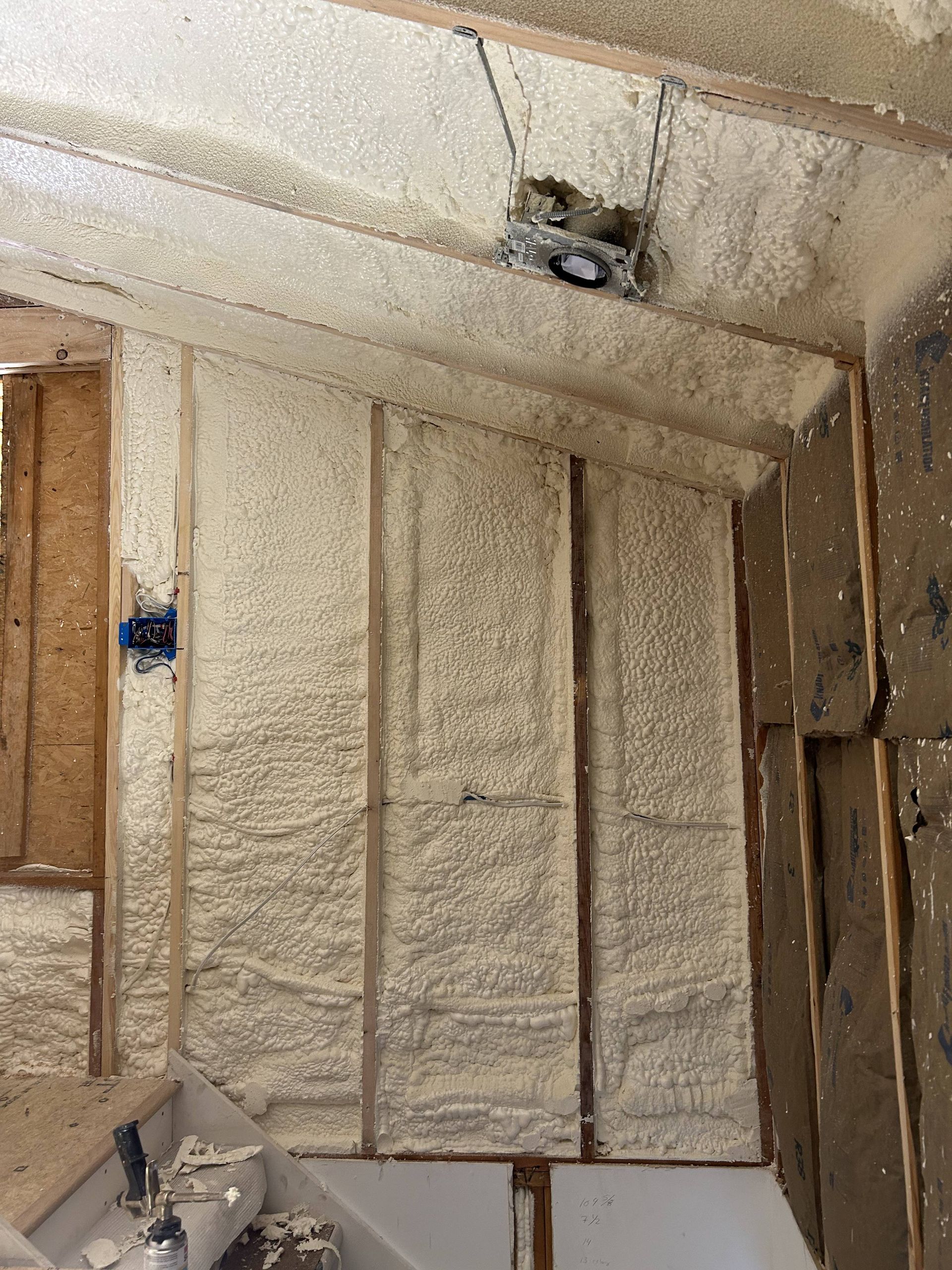 Interior wall under construction with spray foam insulation and exposed wooden framing.