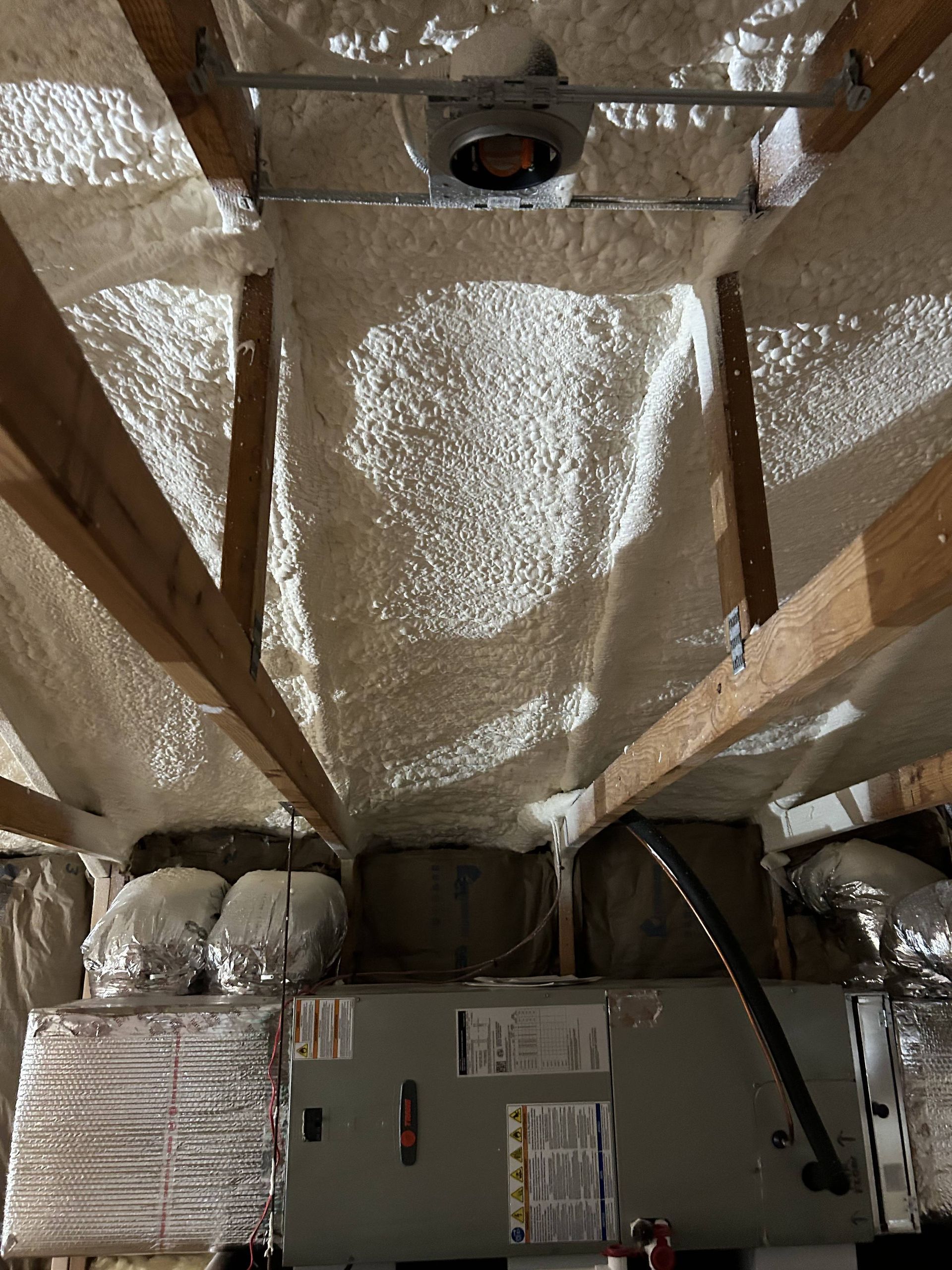 Foil-lined attic with exposed rafters, insulation, ducting, and HVAC equipment.