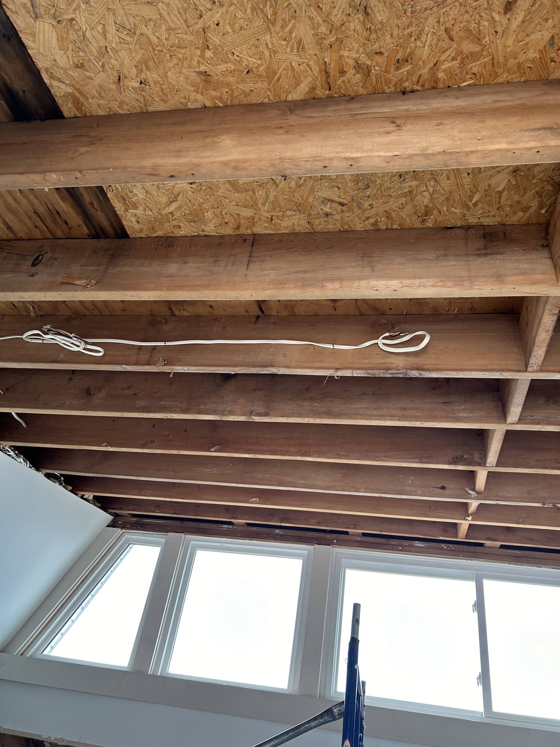 Exposed wooden ceiling beams above bright windows, with a blue pole in the foreground
