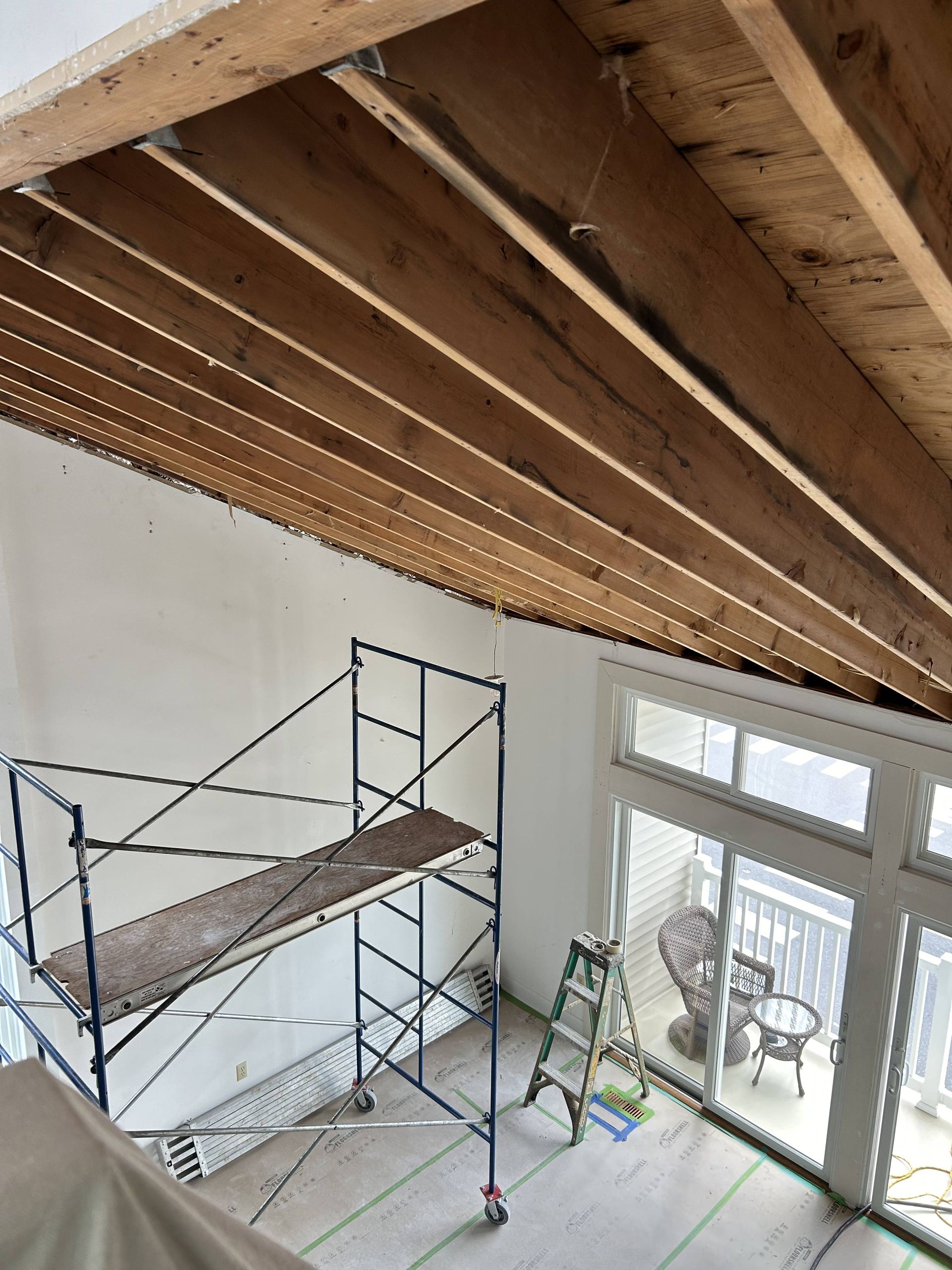 Loft room with exposed wooden ceiling beams, scaffolding, and glass doors to a balcony.