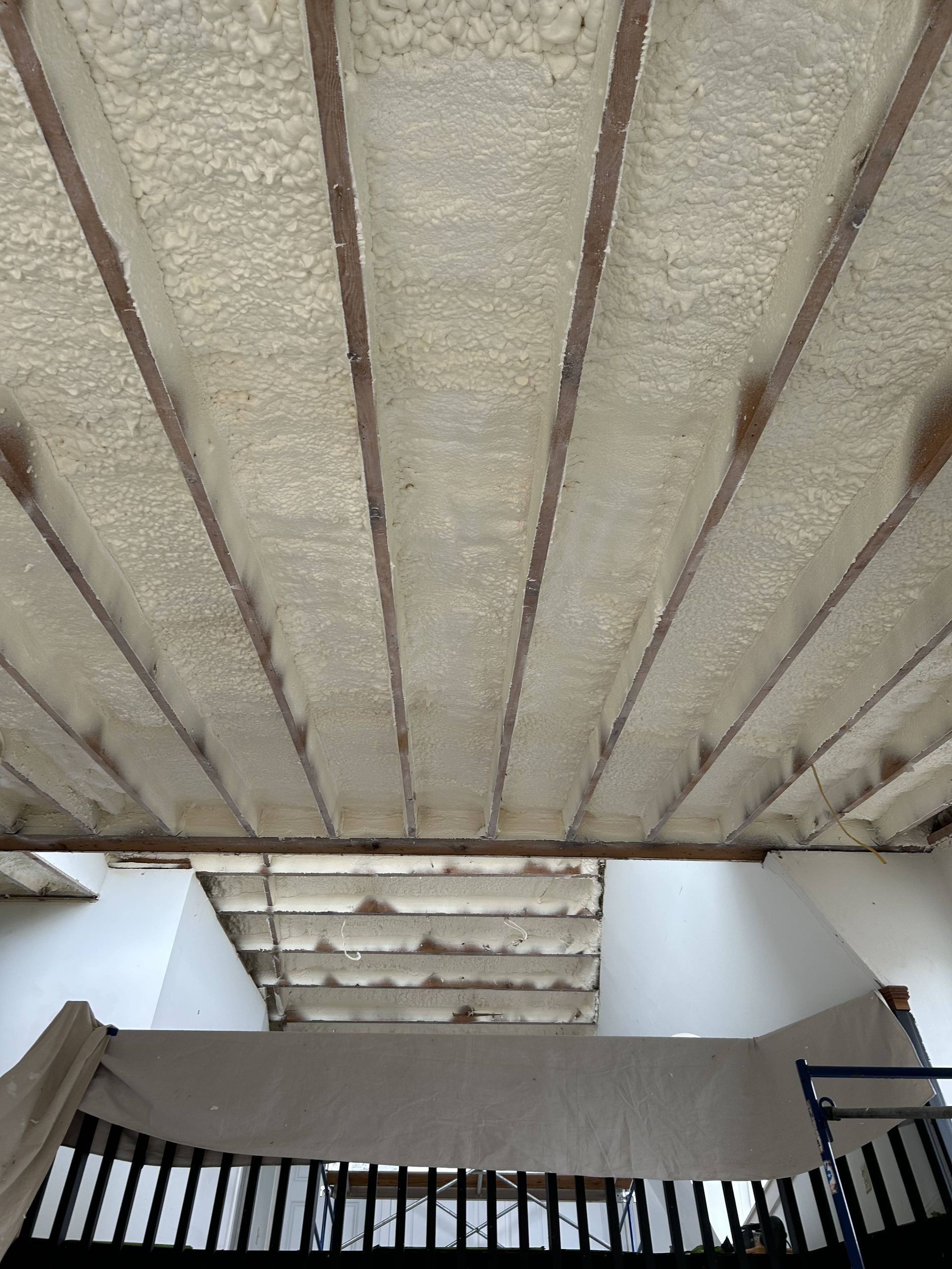 Covered stairwell with concrete ceiling, white walls, and a black railing below.