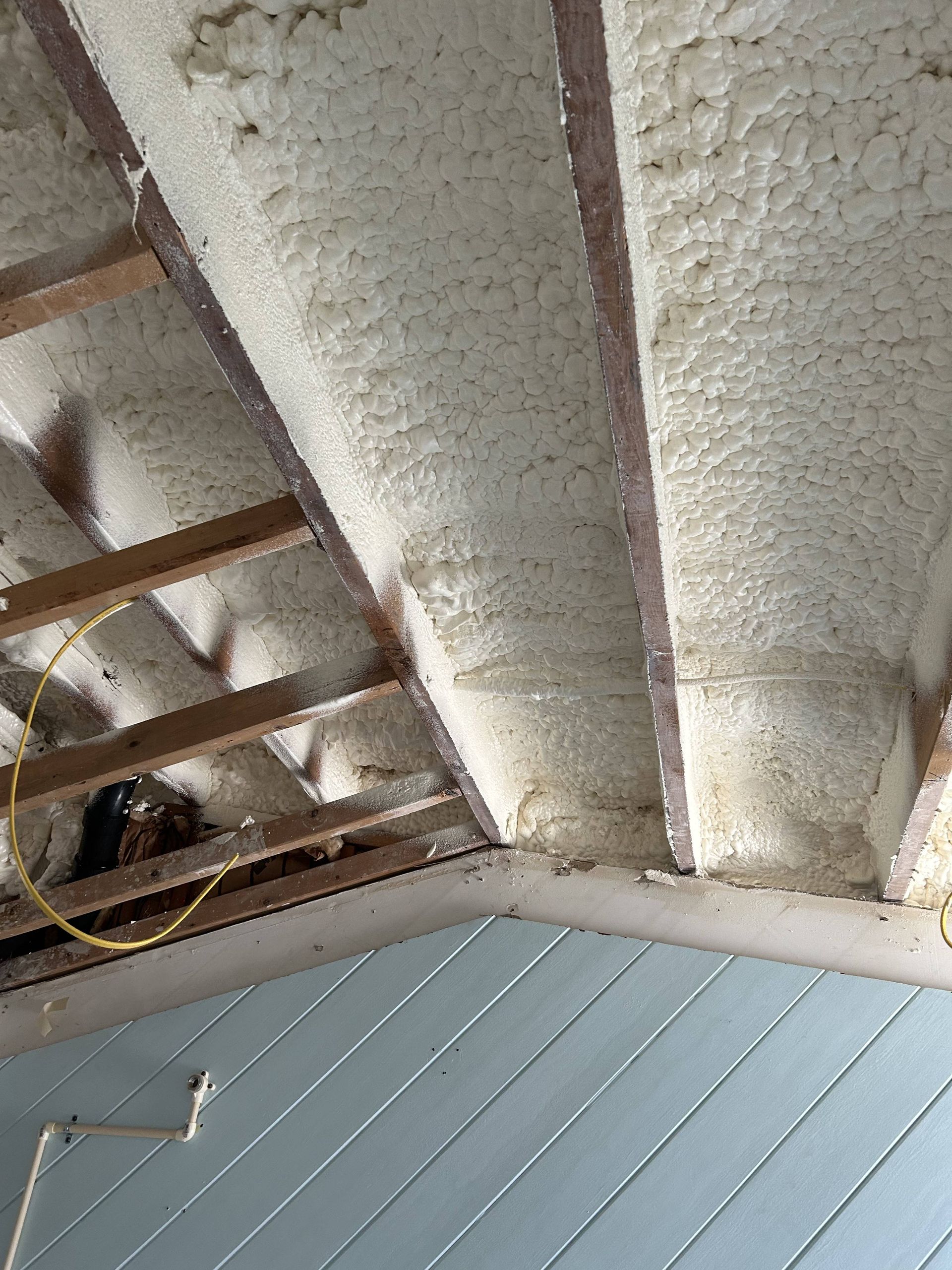 Partially demolished ceiling with exposed wooden beams and white insulation above a blue paneled wall