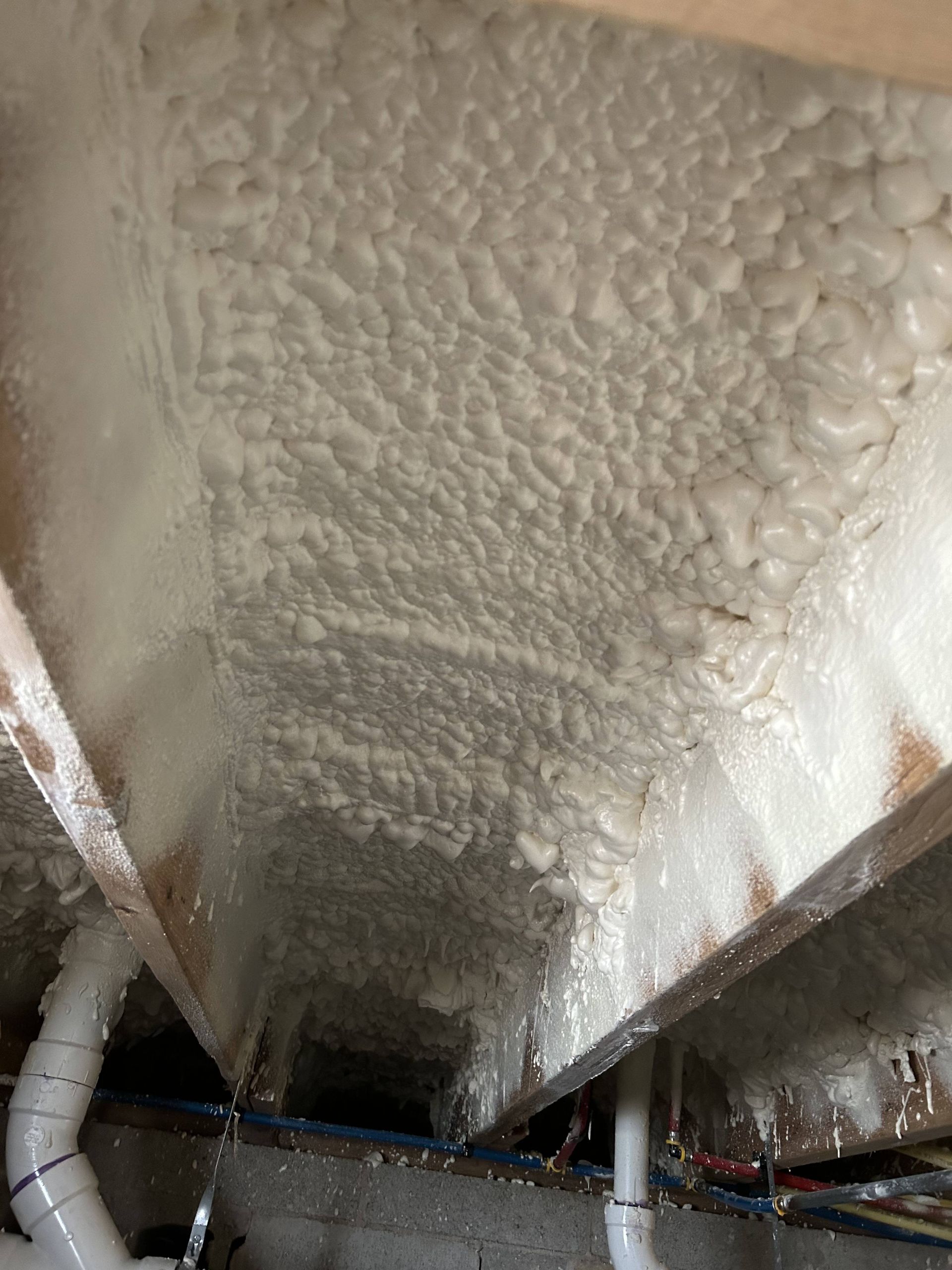Spray foam insulation coating a basement ceiling with exposed pipes and joists